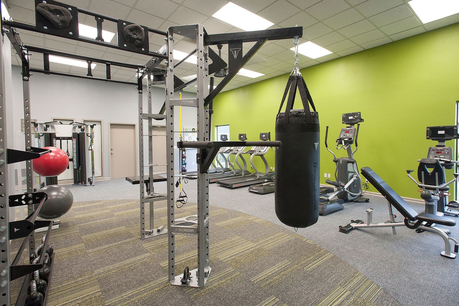 Interior of a resident gym with a weight rack, punching bag, and cardio machines.