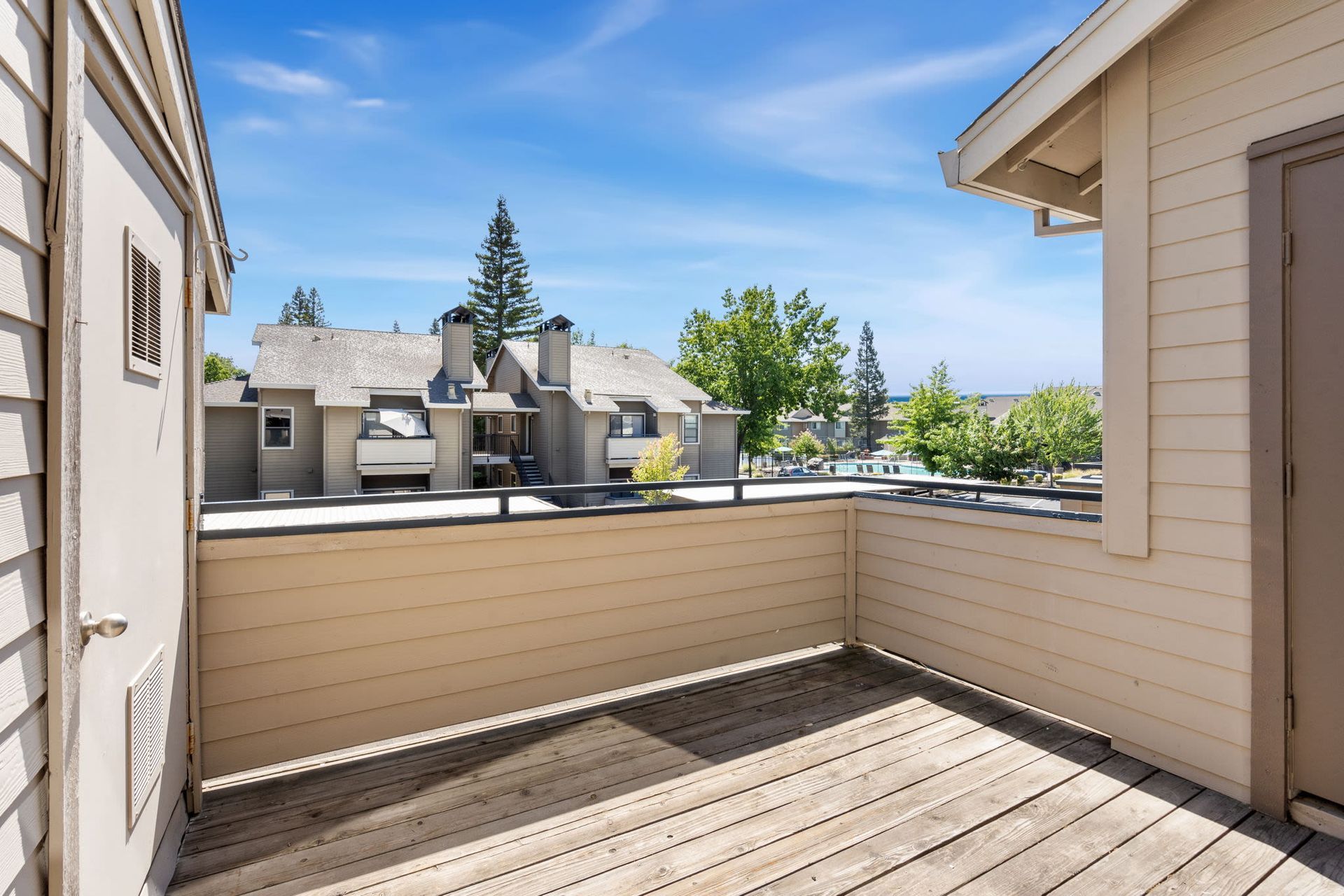 Balcony view of neighboring apartment buildings and a pool area under a blue sky.