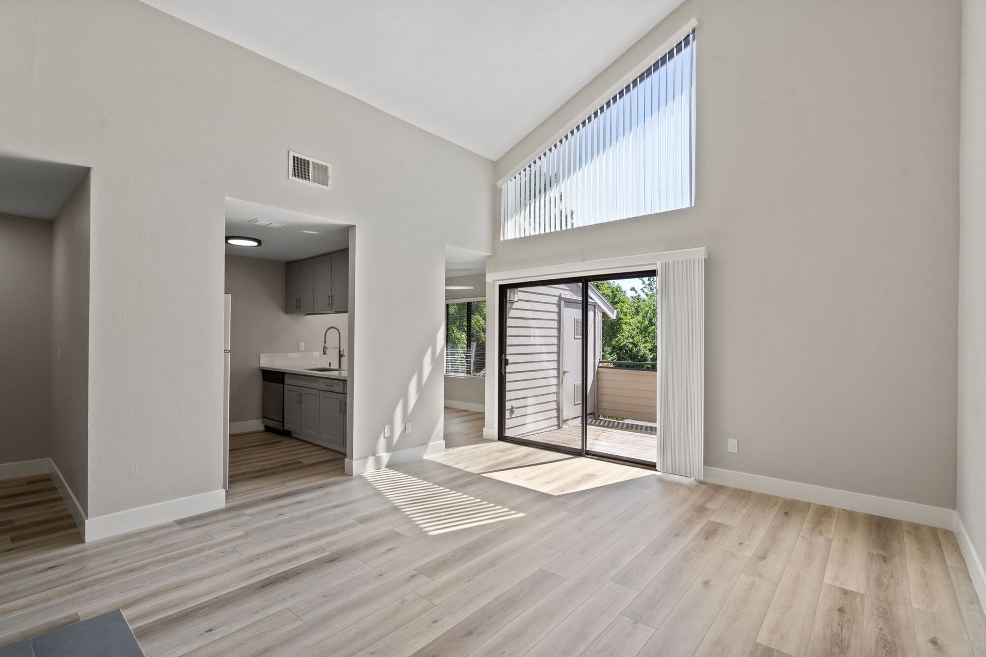 Open living area with vaulted ceiling, kitchen, and sliding glass door to a balcony.