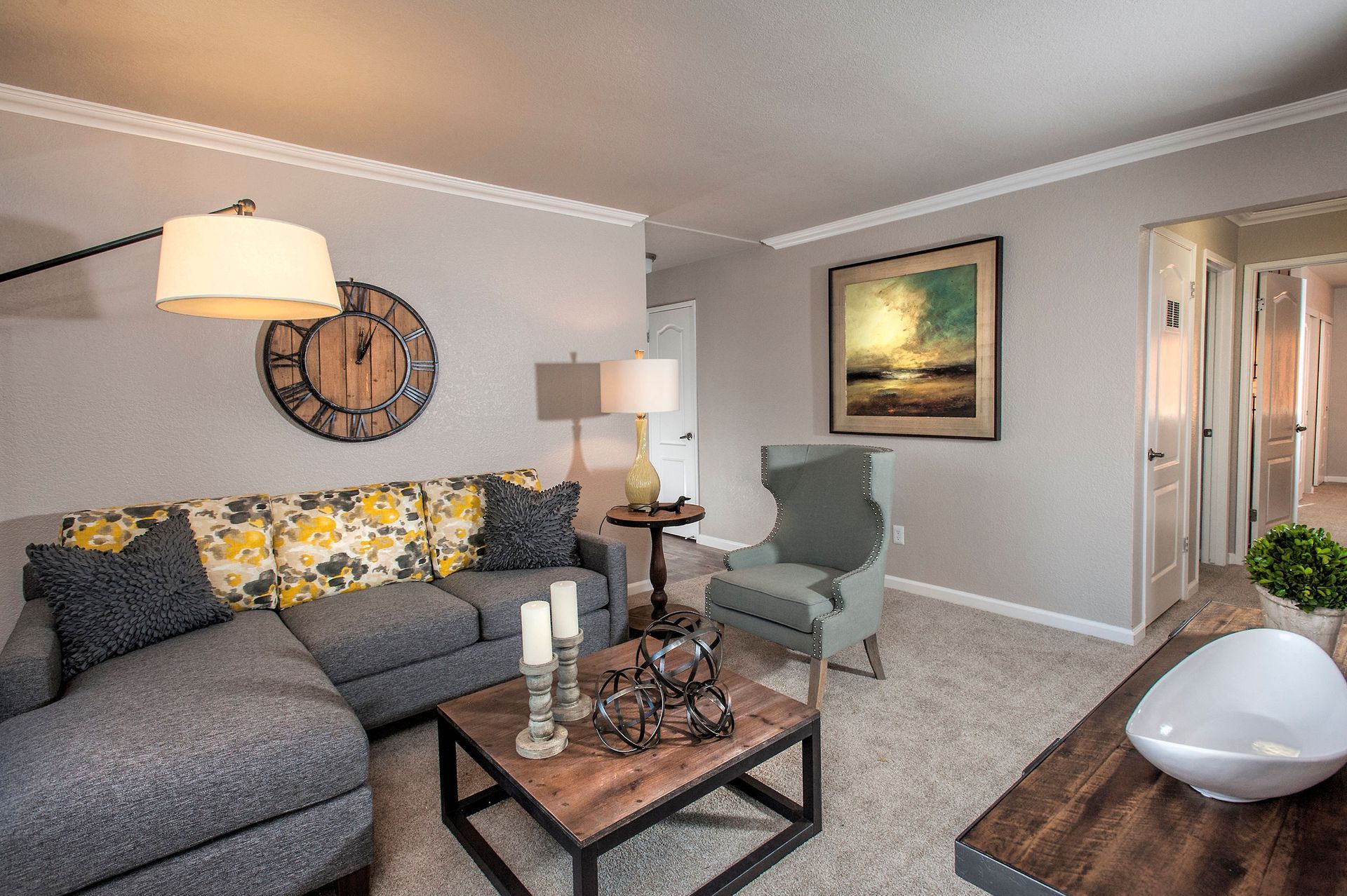 Living room in a model apartment with a gray sectional, patterned pillows, coffee table, and wall art.