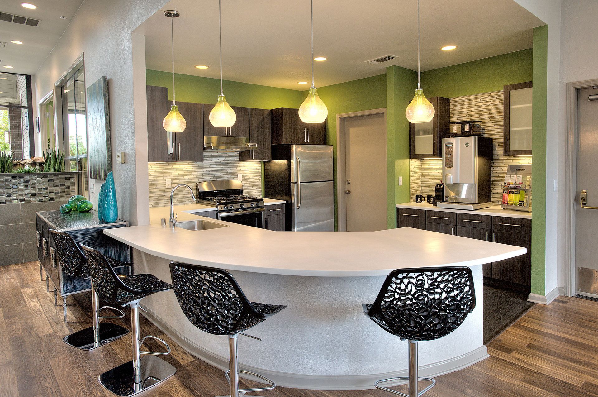 Modern community kitchen with curved white island, pendant lights, and stainless steel appliances.
