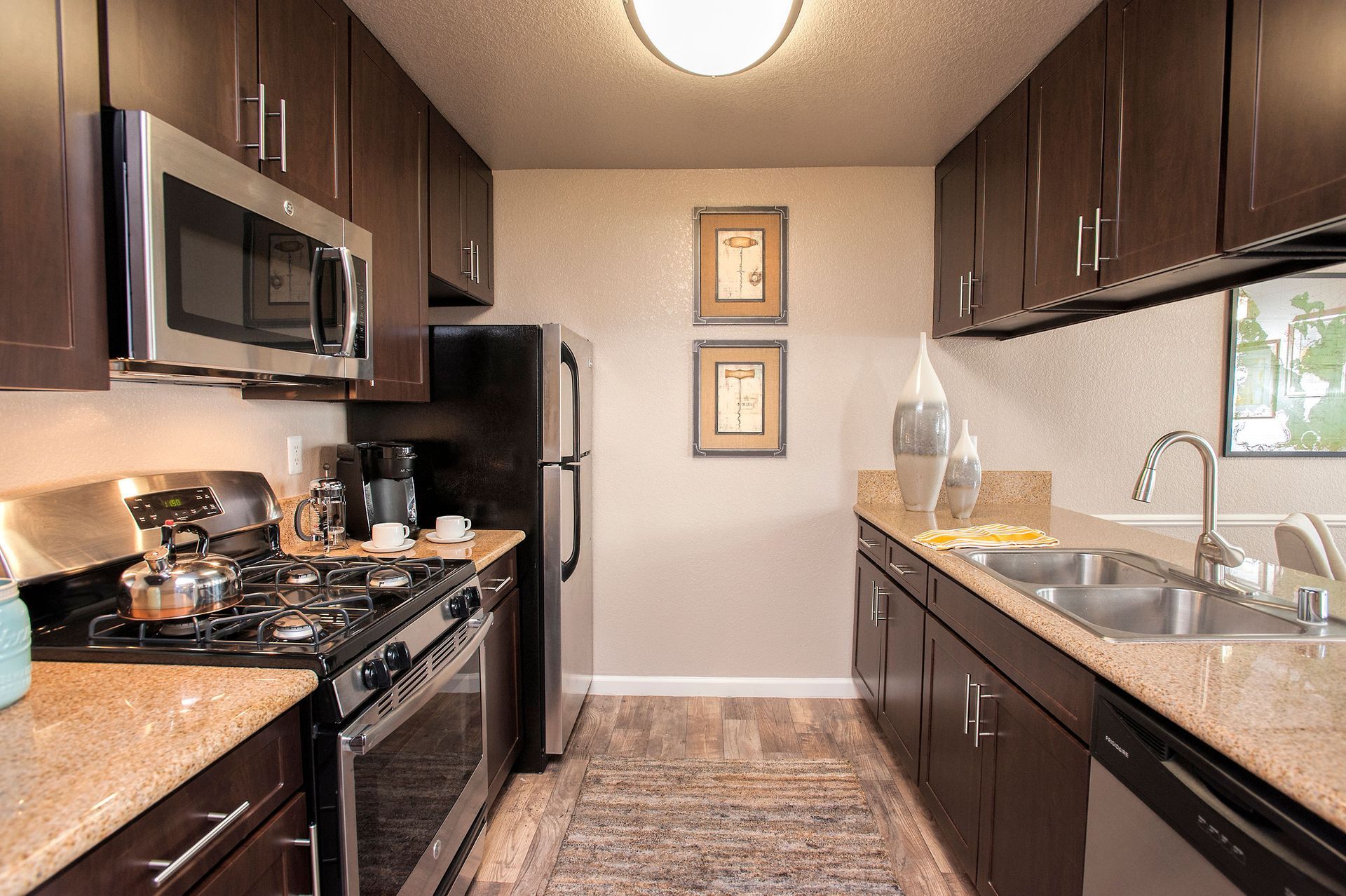 Galley-style kitchen with dark wood cabinets, stainless steel appliances, and a double sink.