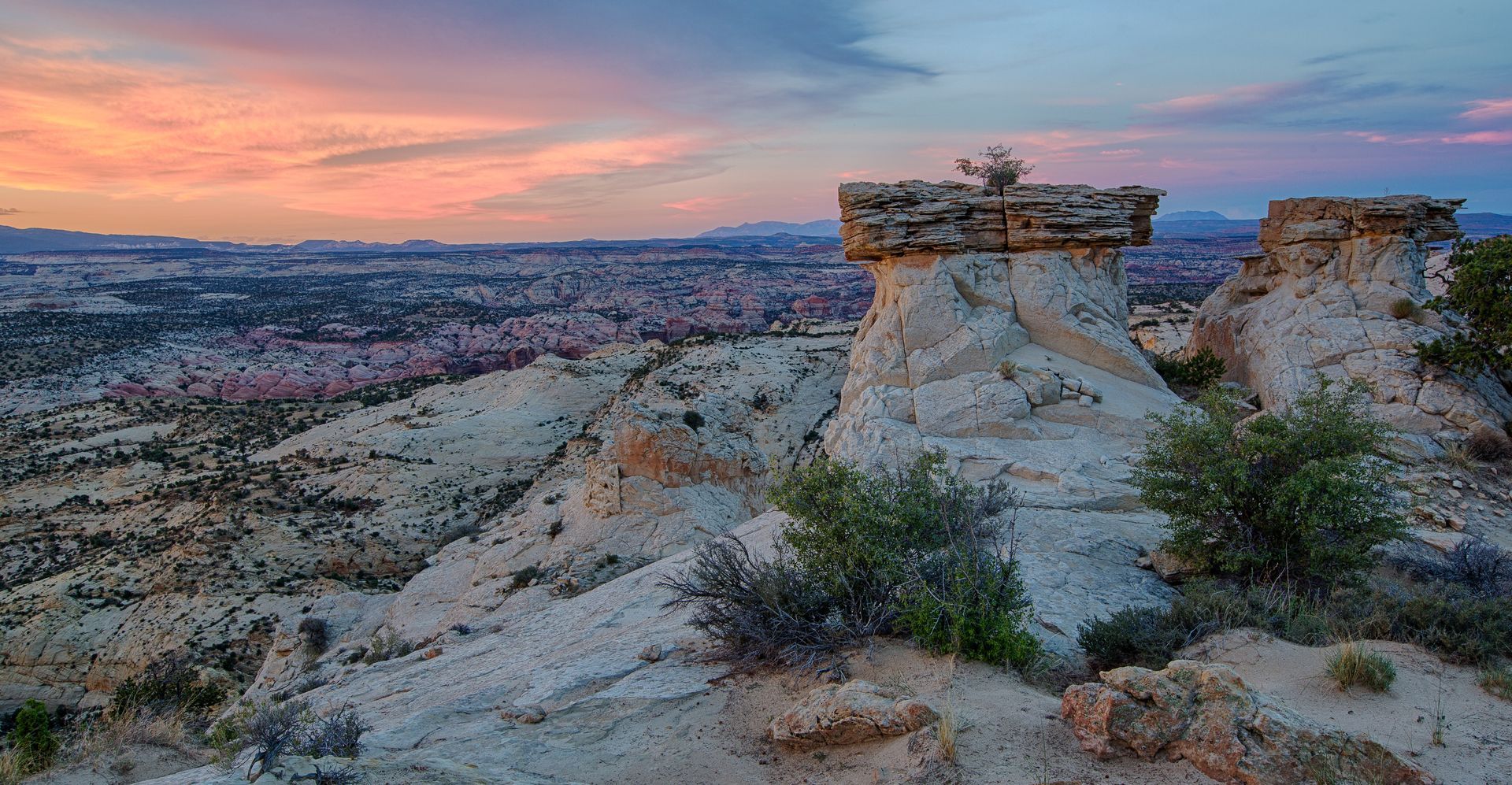Desert landscape at sunset with sandstone rock formations and colorful sky.