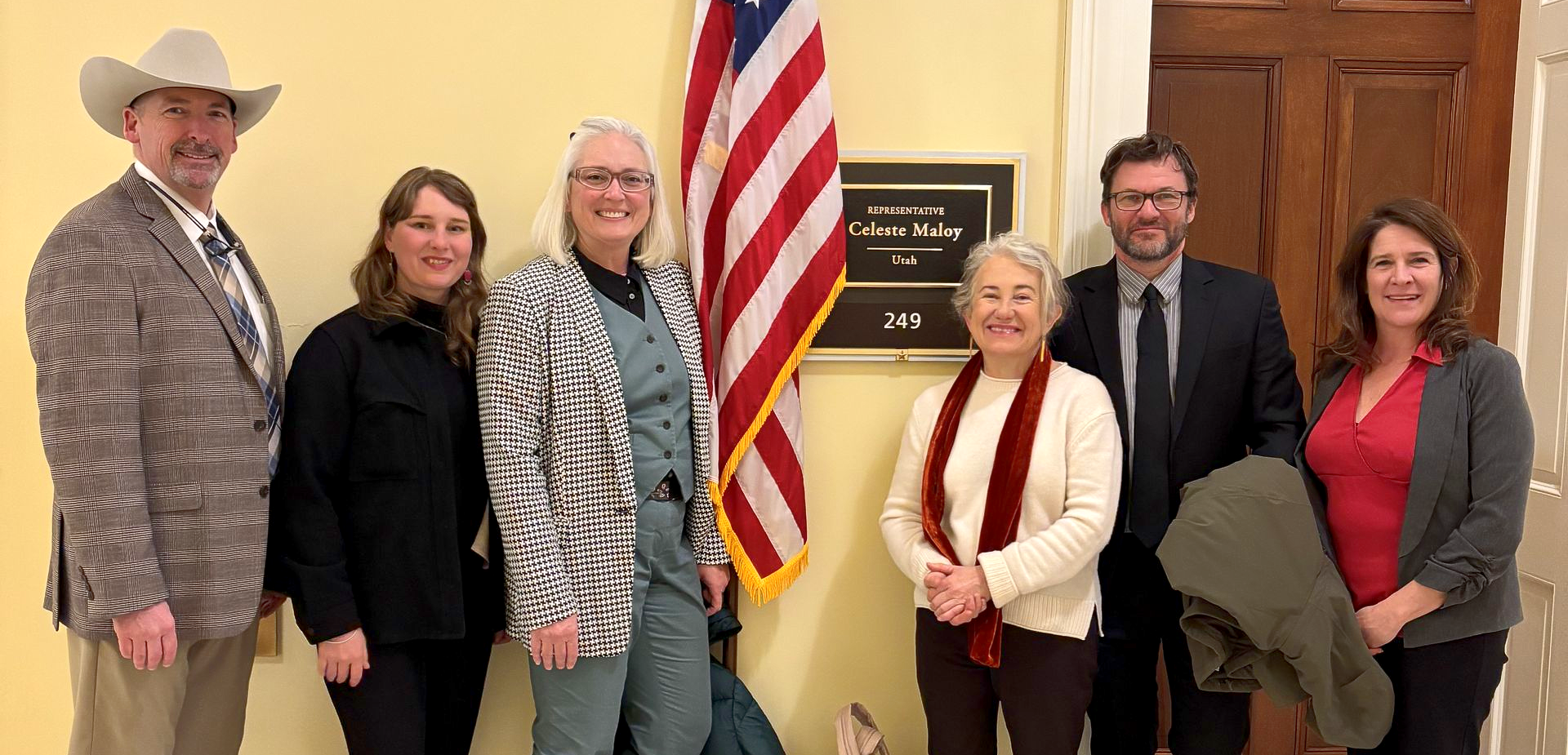 A group of people smile while standing in front of a member of Congress' door in DC.