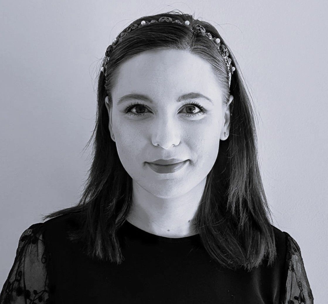 Woman with dark hair, wearing a pearl headband, in black top, looking at the camera.