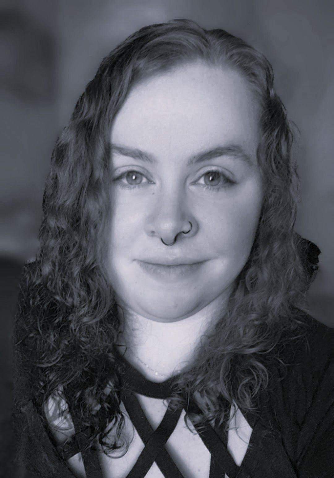 Woman with curly hair and nose ring, smiling. Wearing a dark top with a geometric pattern.
