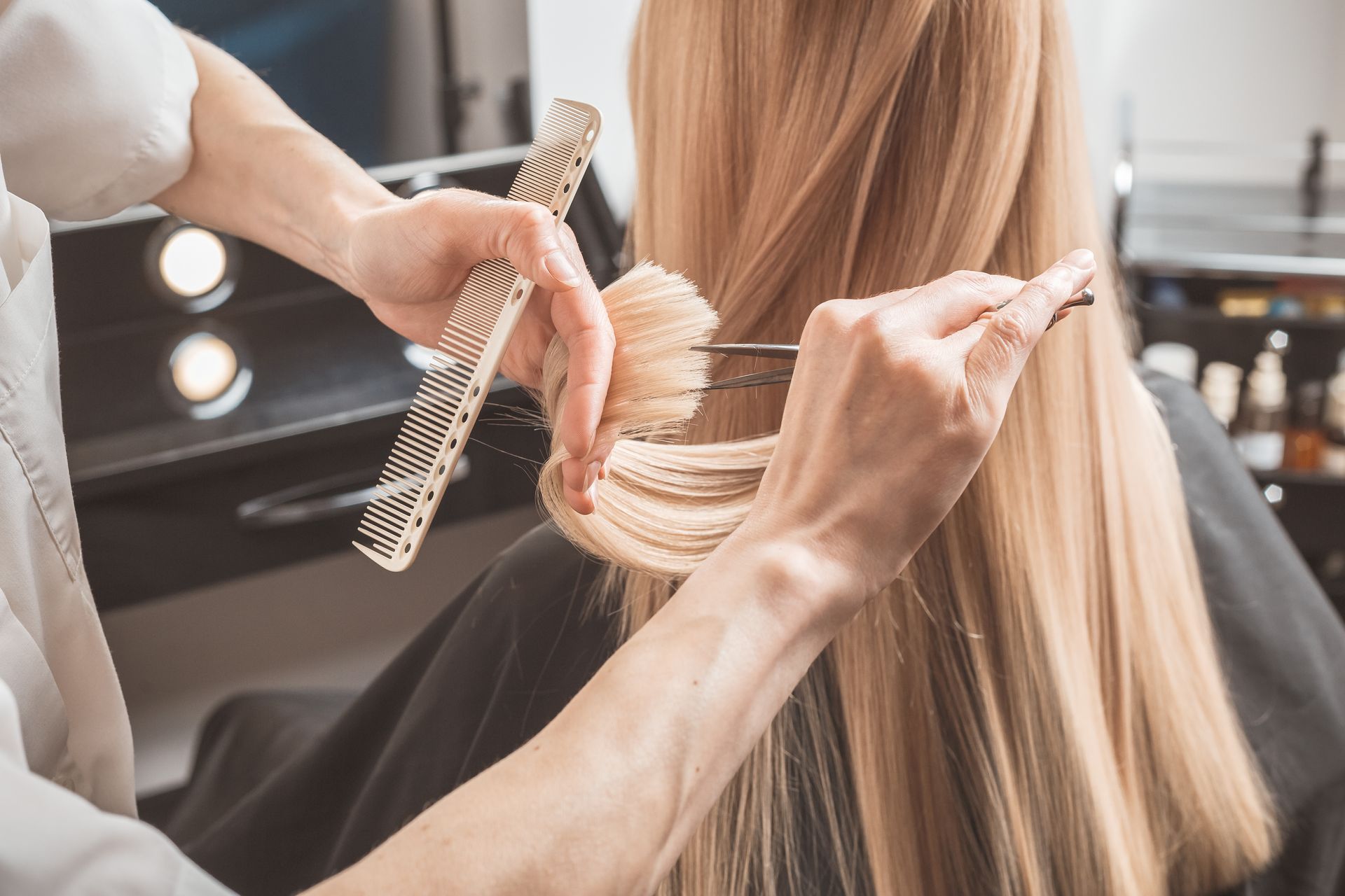 Stylist cutting long blonde hair with scissors and a comb in a salon.