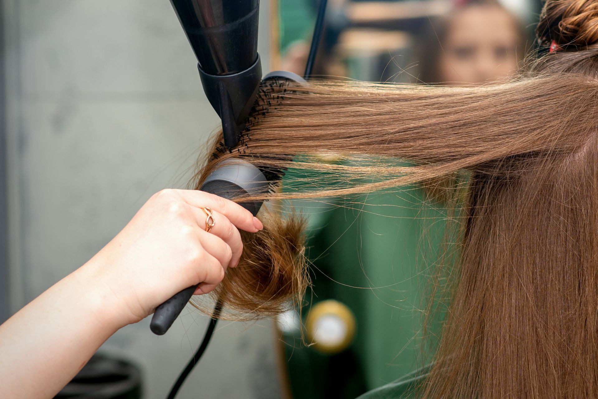 Stylist blow-drying and brushing long hair in a salon.