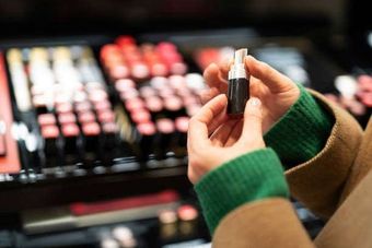 A woman is holding a lipstick in her hands in front of a display of lipsticks.