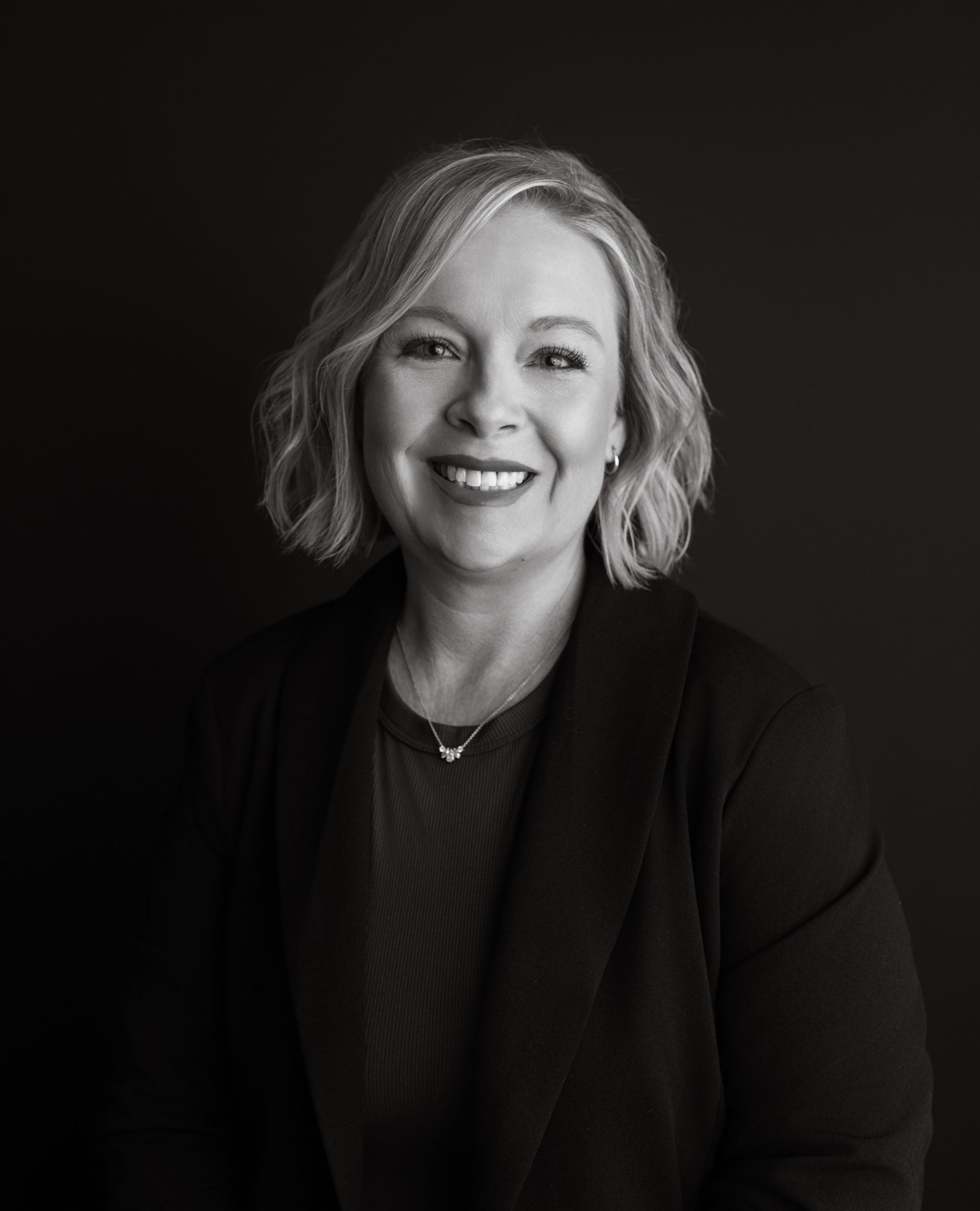 Woman with short gray hair smiles, wearing a black blazer and dark shirt.