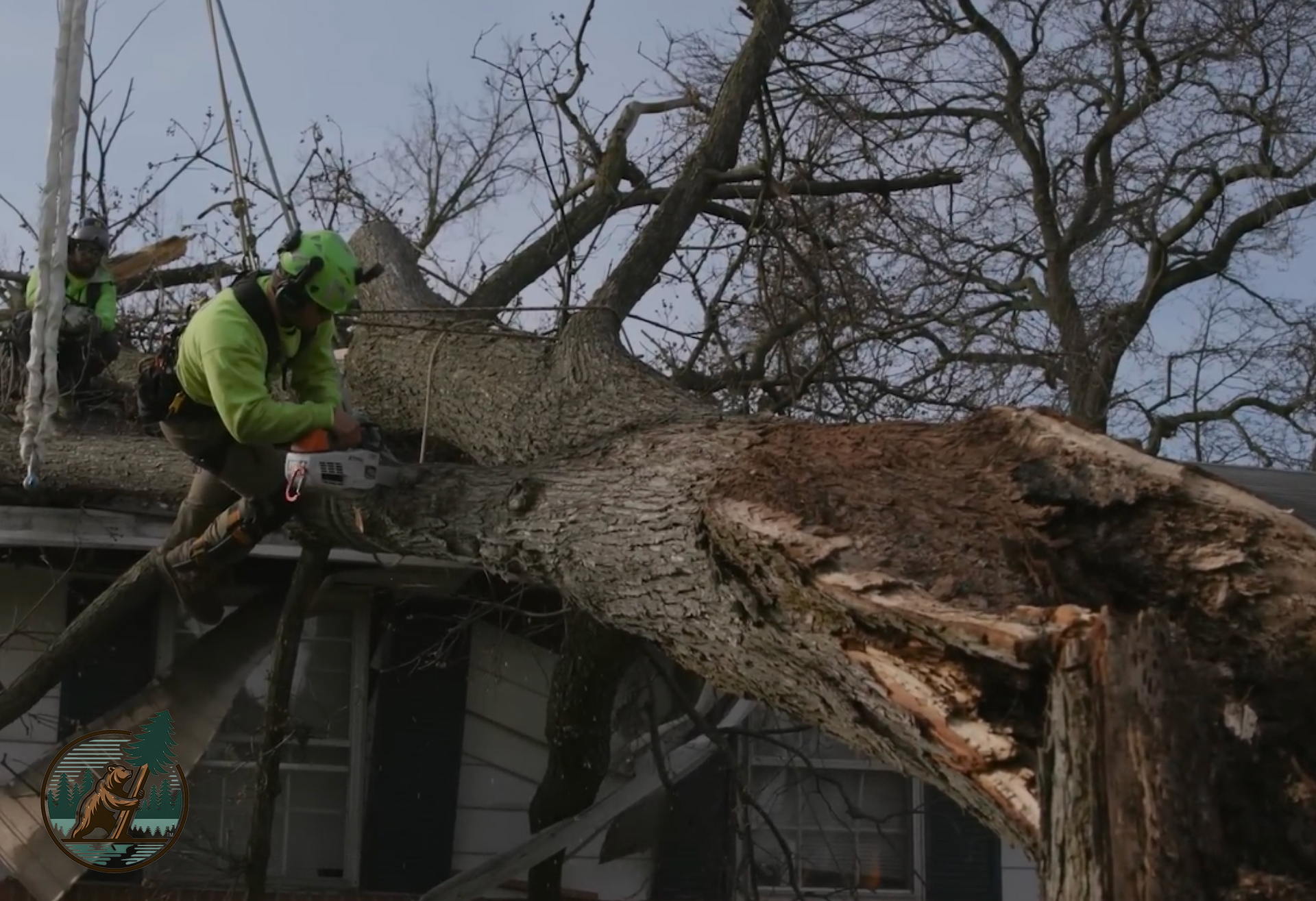 Two arborists from Big Bear Lake Tree Service cutting away branches from a tree that fell on a resident's home in Running Springs, CA, after a storm.