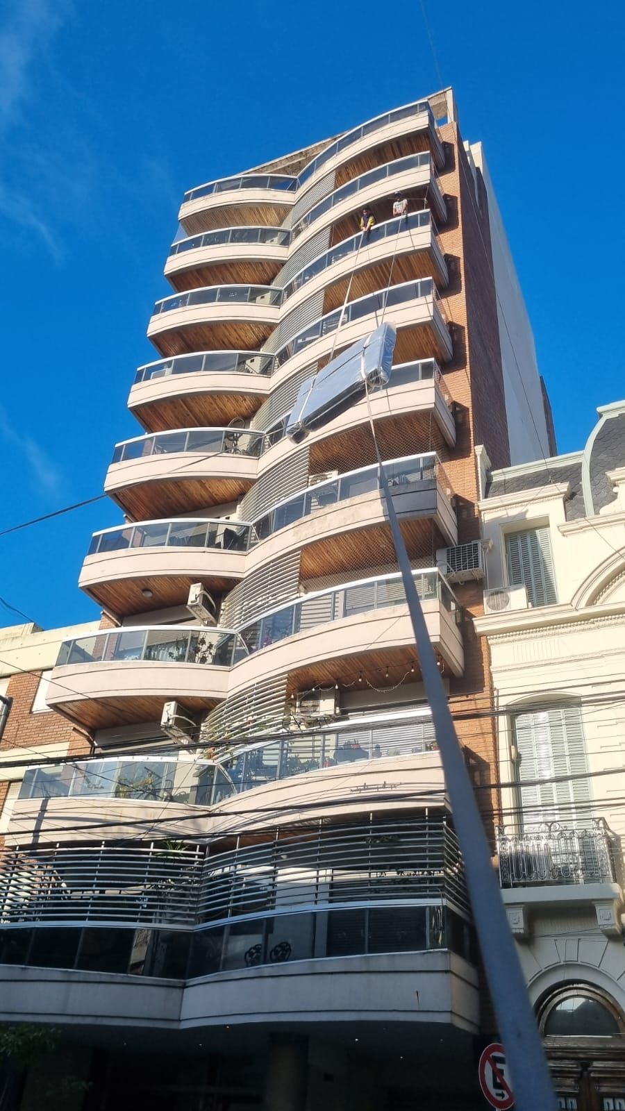 Edificio de apartamentos de varios pisos con balcones curvos bajo un cielo azul claro.
