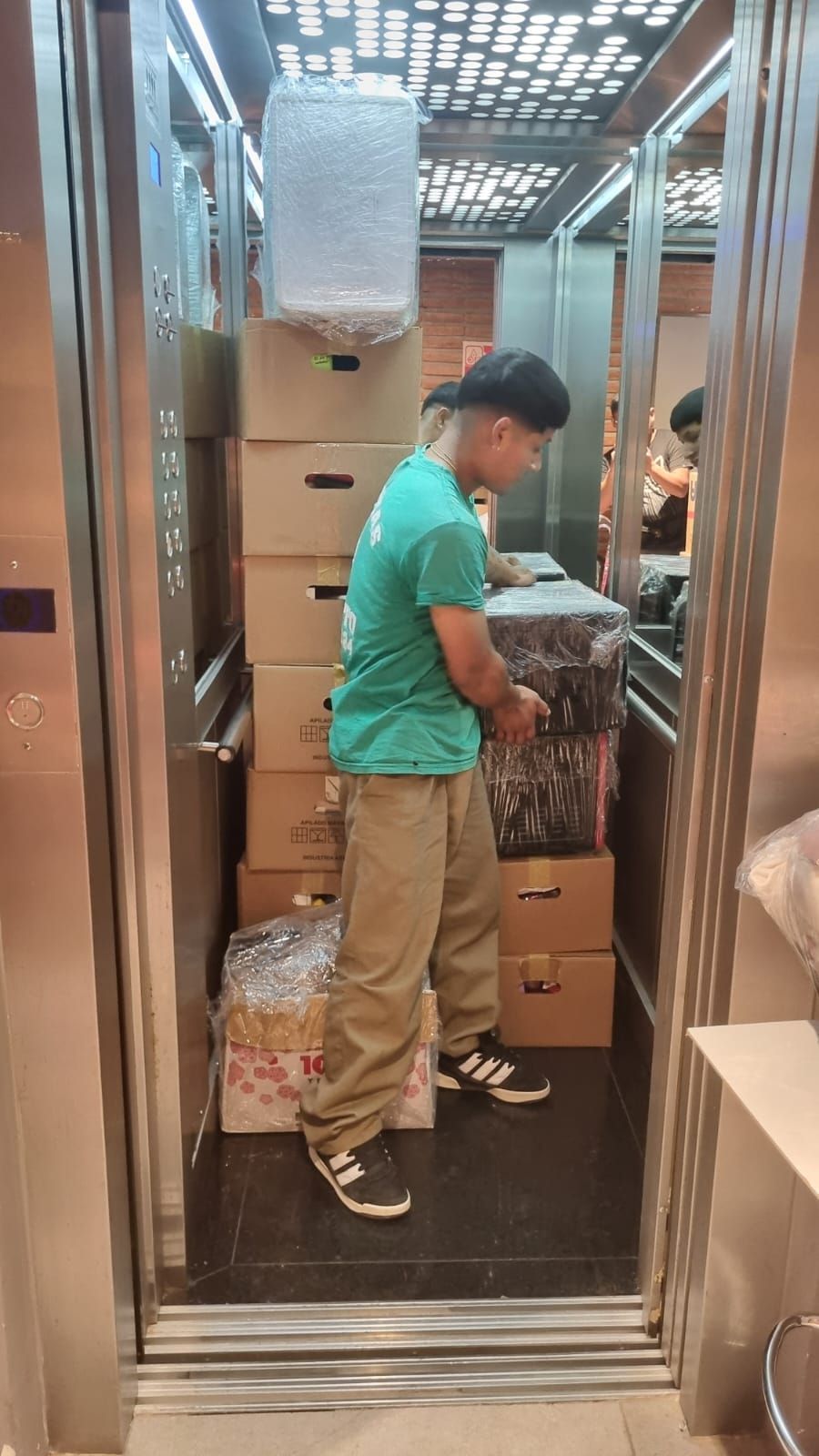 Un hombre con camisa verde carga cajas y artículos envueltos en un ascensor.