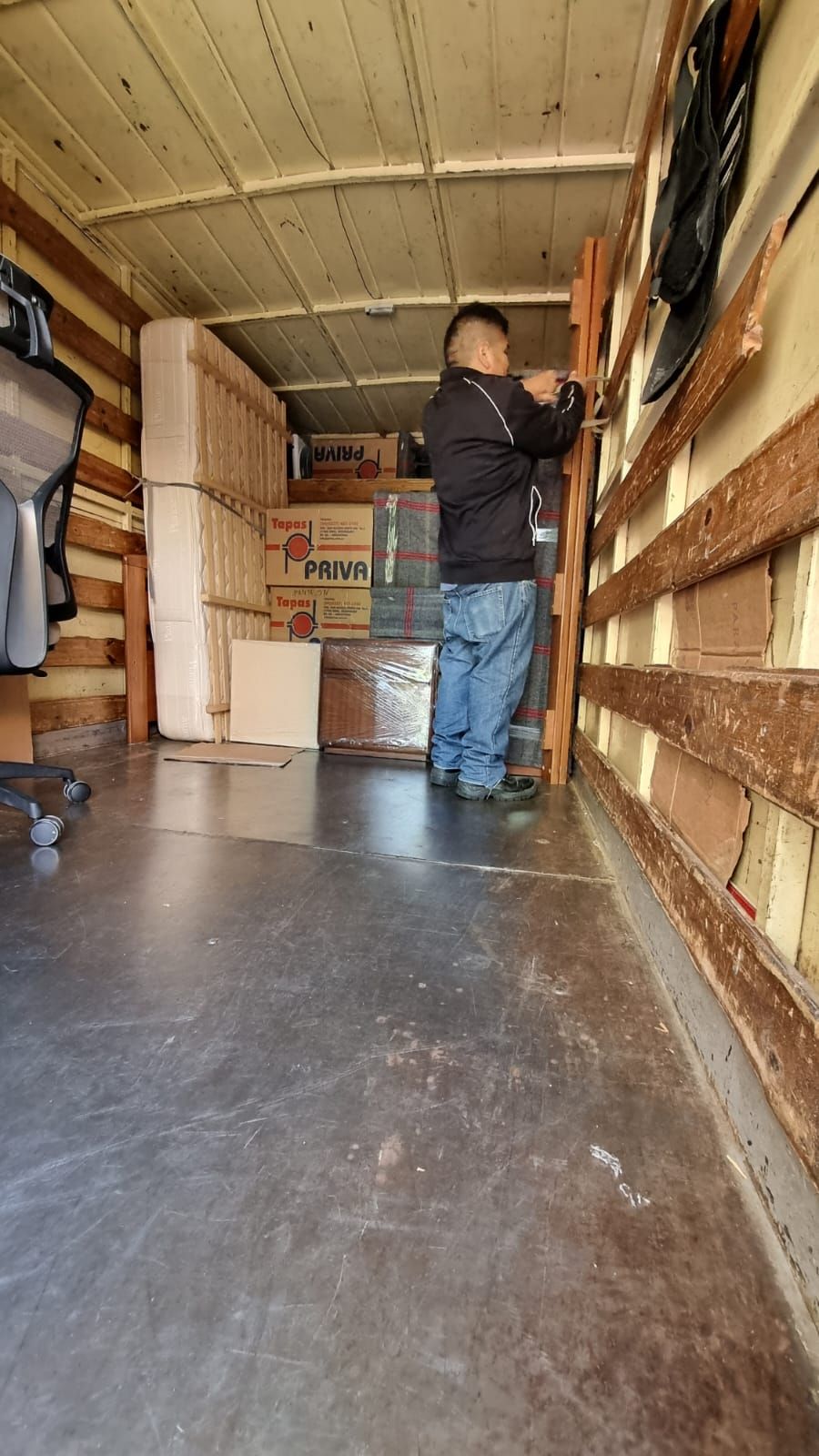 Persona en un camión instalando tablones de madera. El interior del camión contiene cajas y otros artículos.
