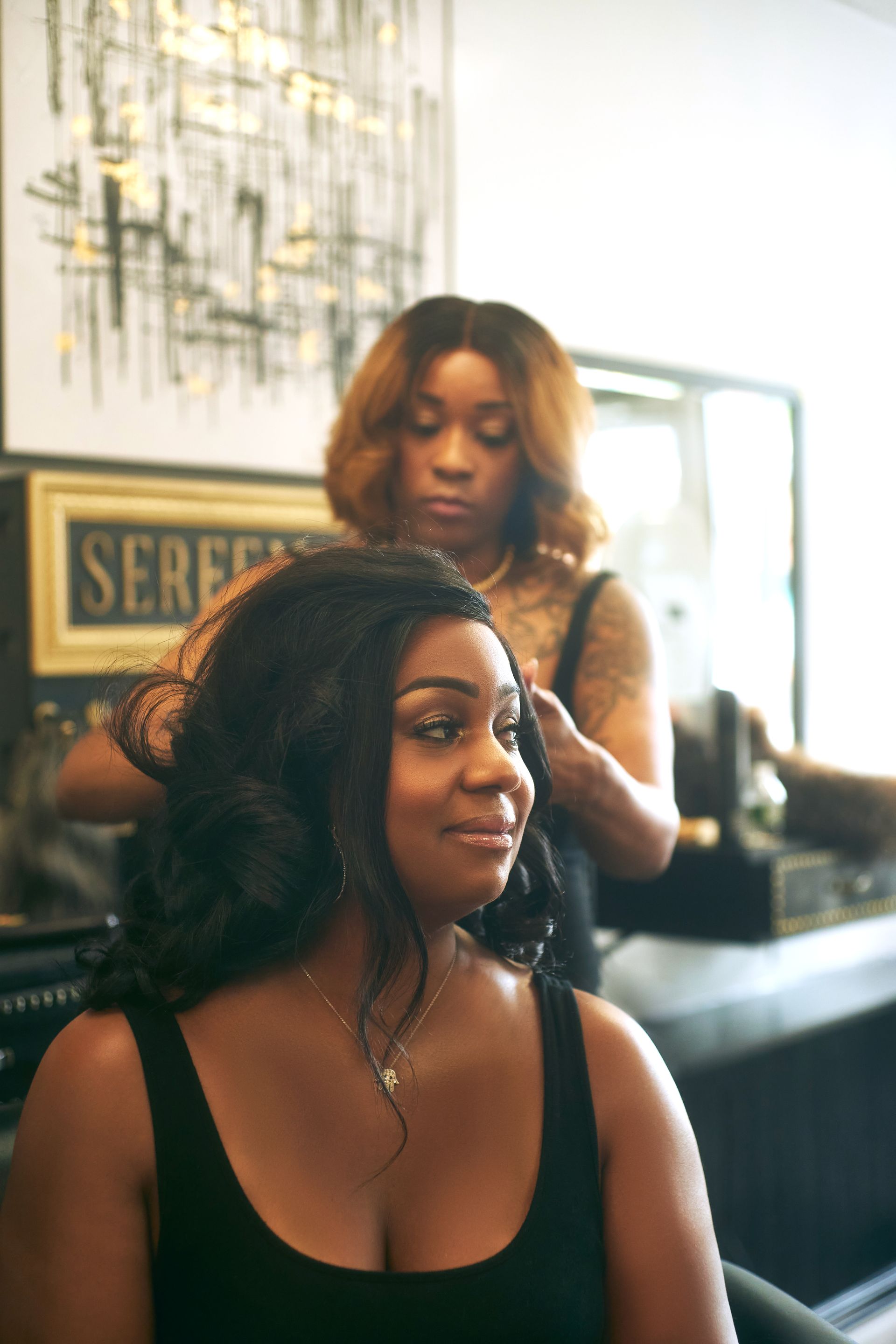 Woman getting her hair styled by a stylist in a salon. The woman smiles, wearing a black top.