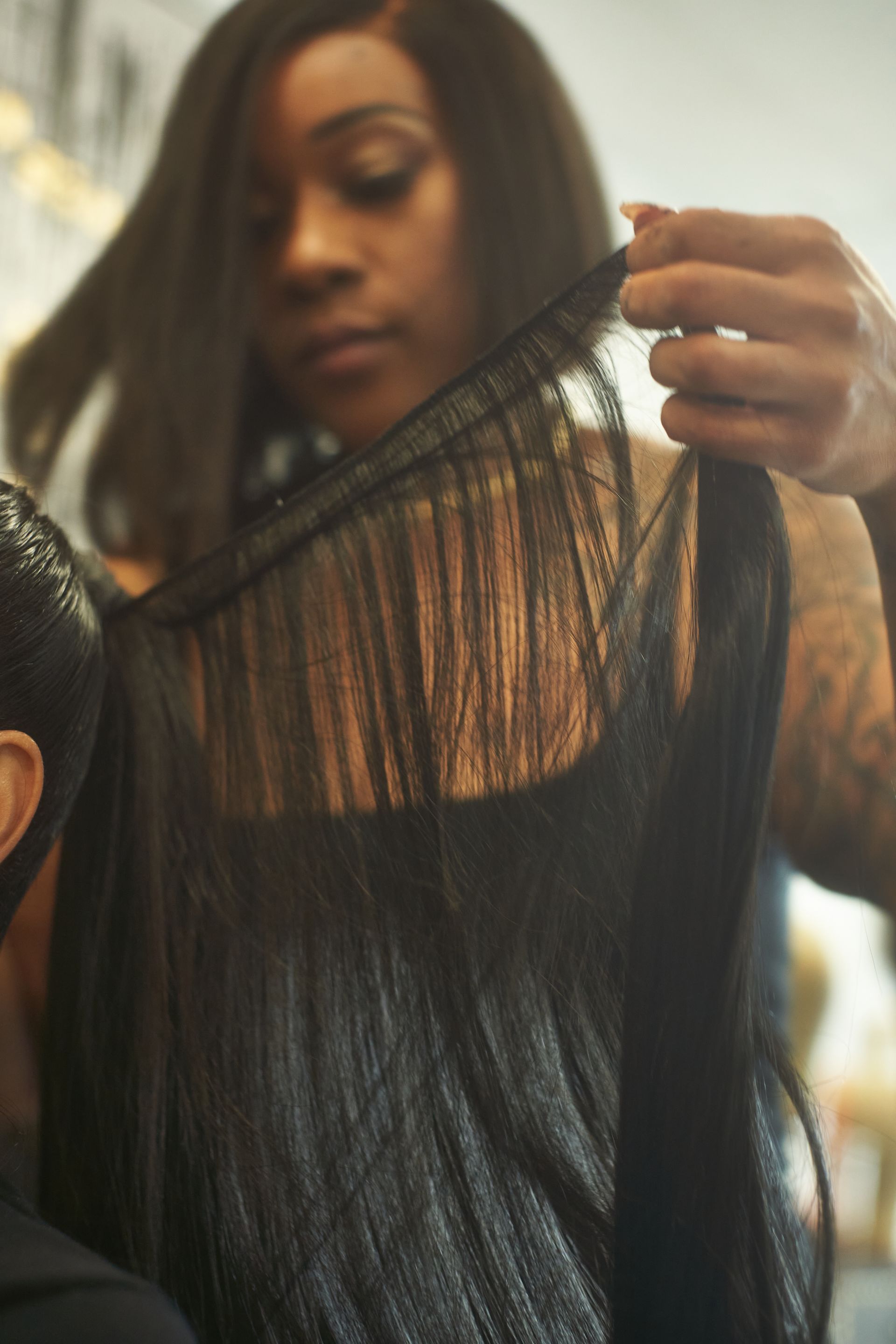 Woman holding and inspecting a black hair weave extension, indoors.
