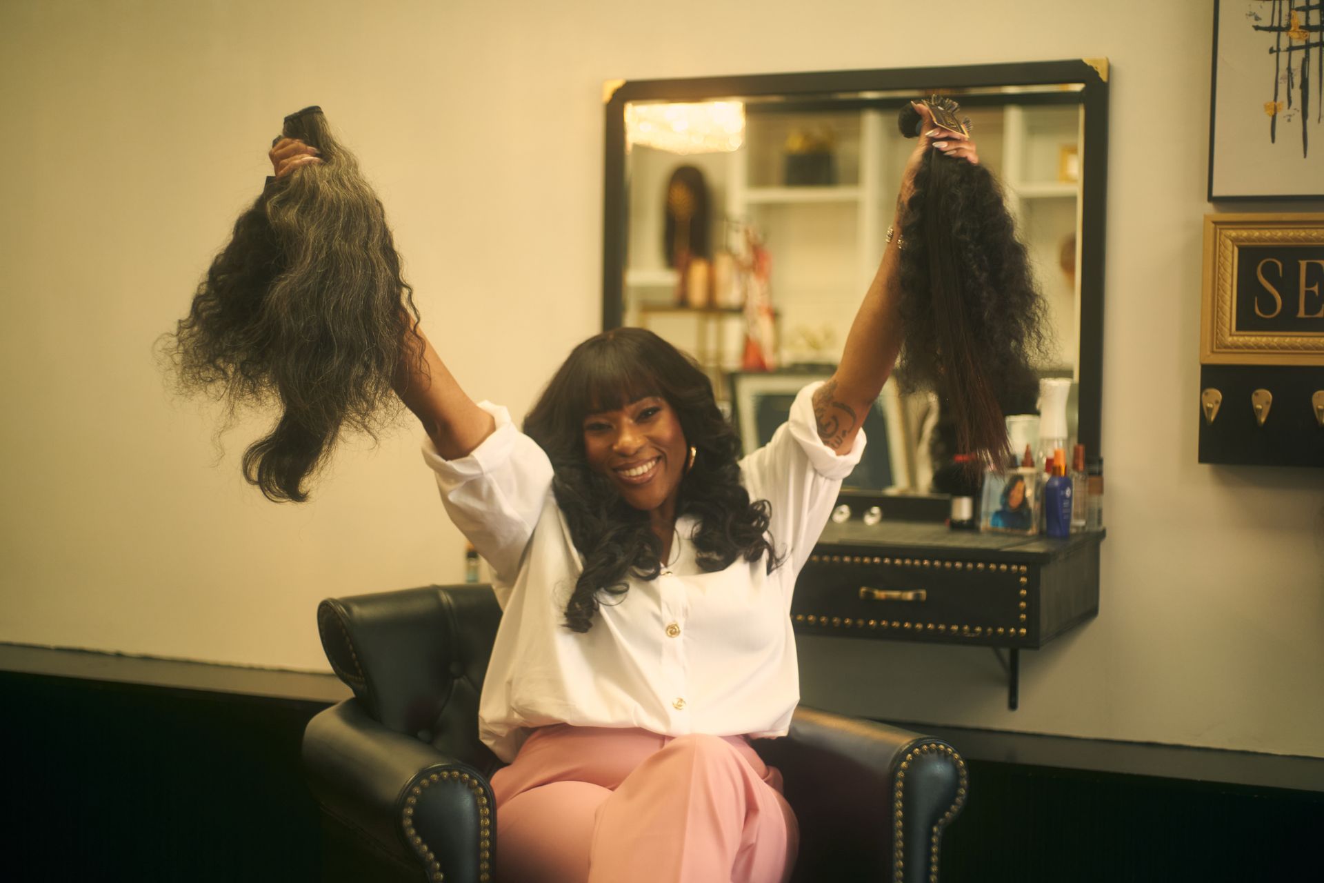 Woman holding up two bundles of dark curly hair, smiling in a salon.