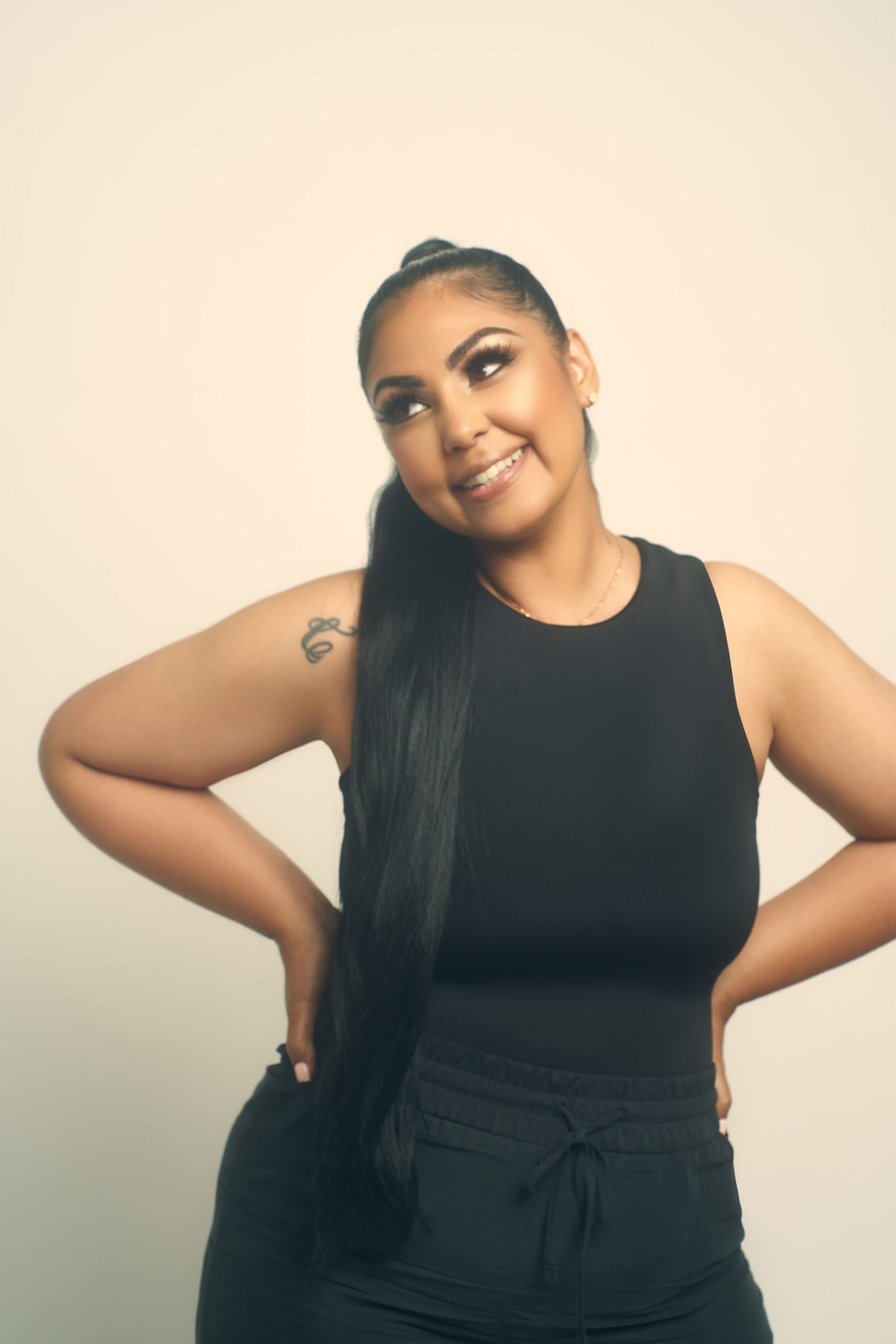 Woman with dark hair in black outfit smiling, posing with hands on hips.