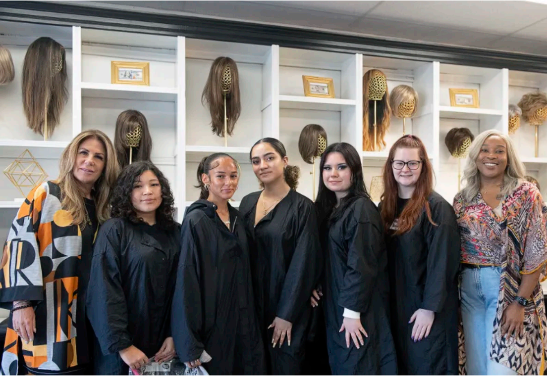 A group of women are posing for a picture in front of a wall of wigs.