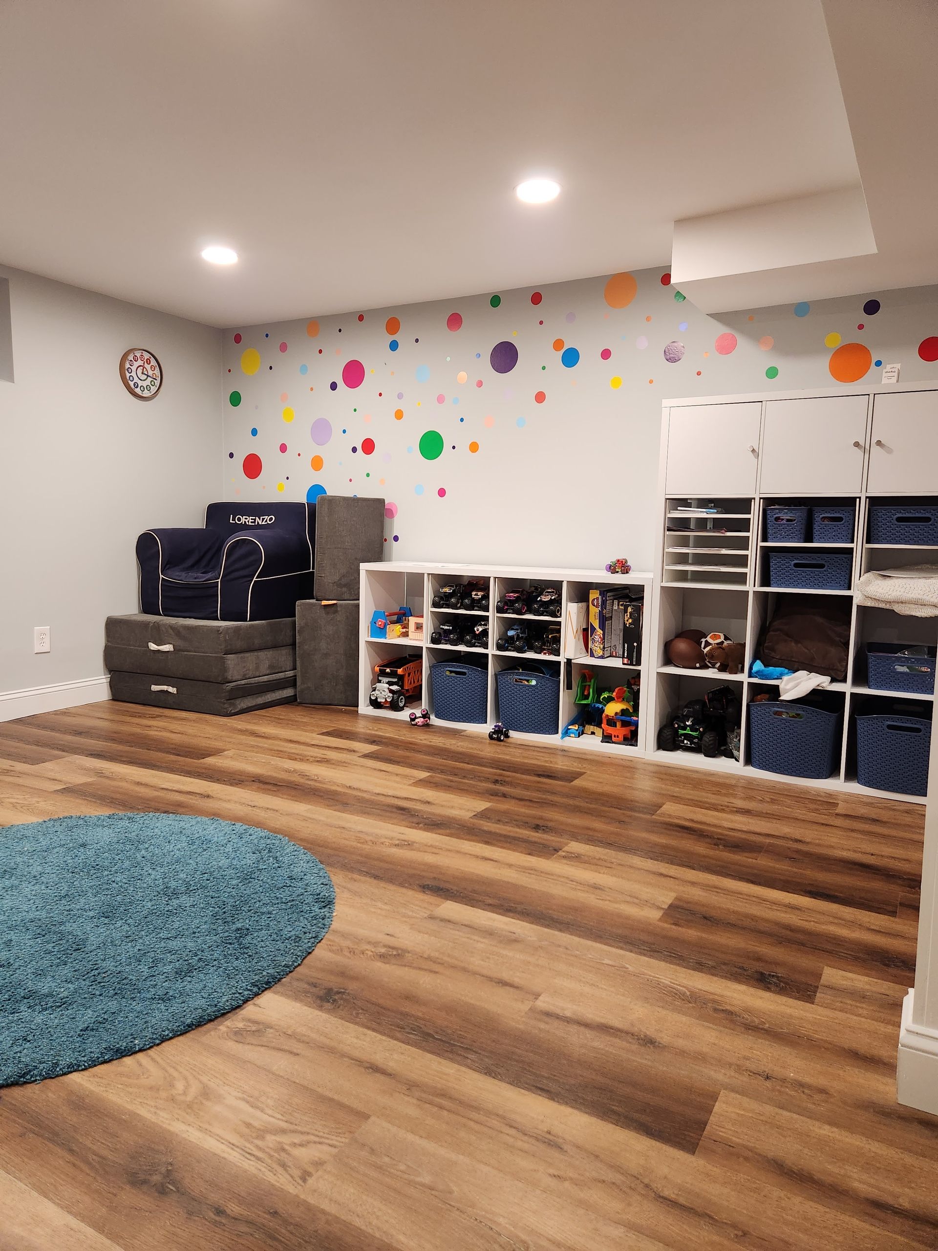 A basement with hardwood floors , shelves , a rug and a clock on the wall.