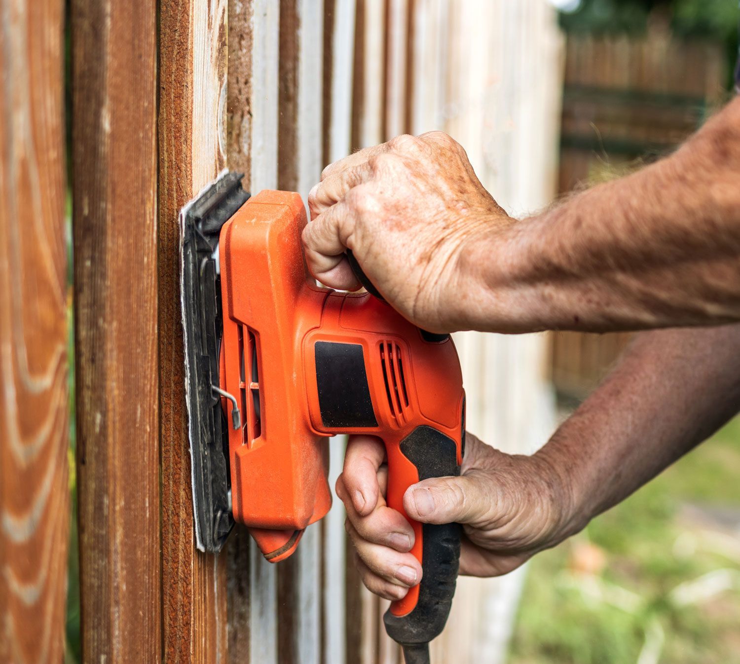 Close-up of male hands repairing wooden fence at backyard