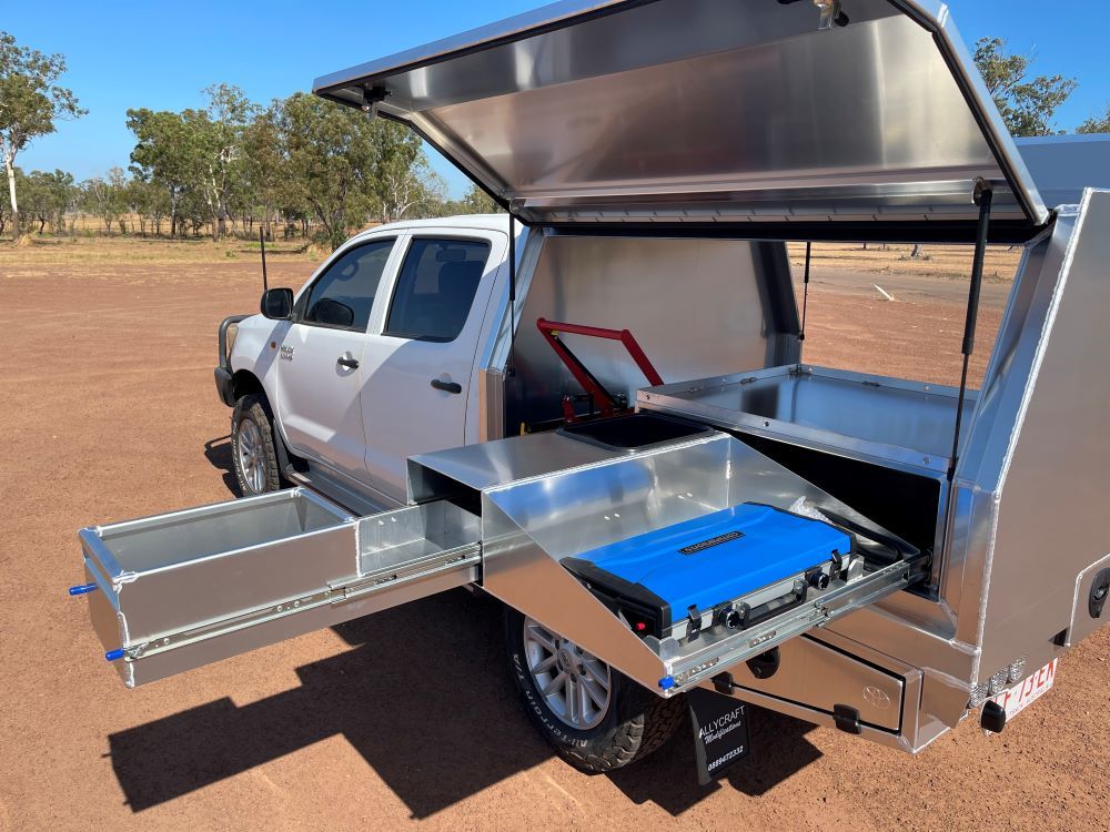 A White Pickup Truck Featuring a Canopy and Built-in Drawers is Stationed in a Dirt Field — Allycraft Modifications in Berrimah, NT