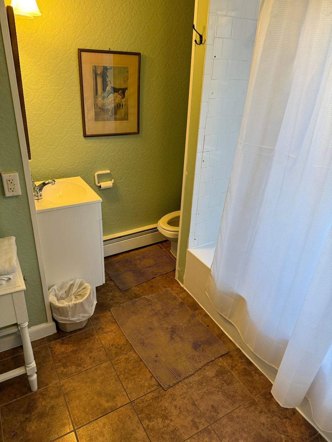 A bathroom with a toilet , sink , shower and picture on the wall.