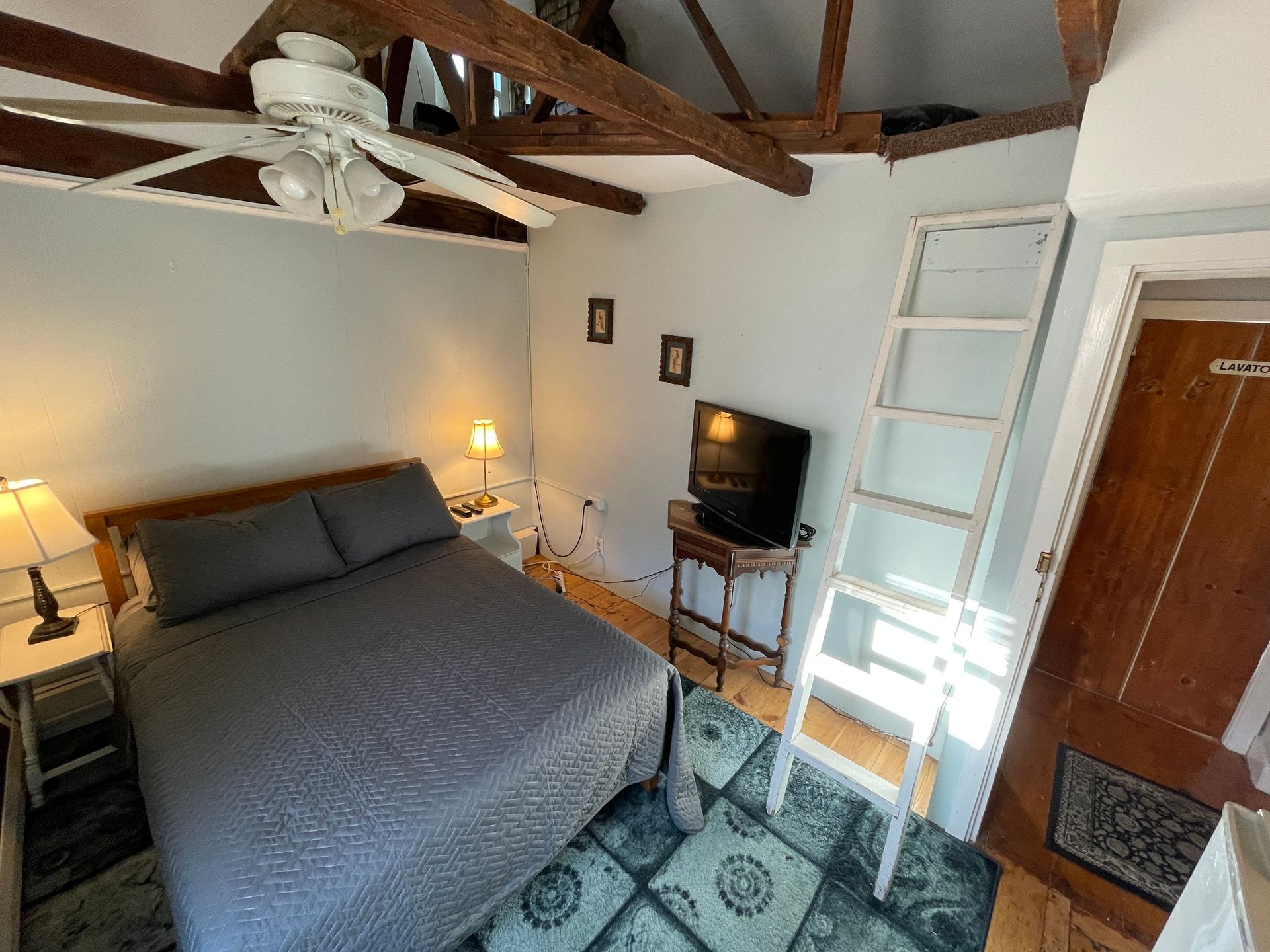 A bedroom with a bed , television , stairs and a ceiling fan.