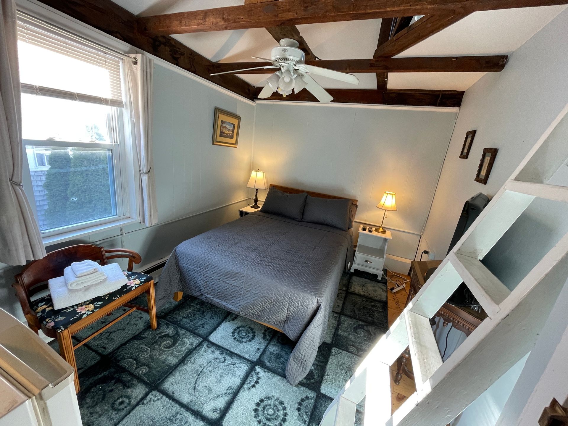 A bedroom with a bed , chair , stairs and a ceiling fan.