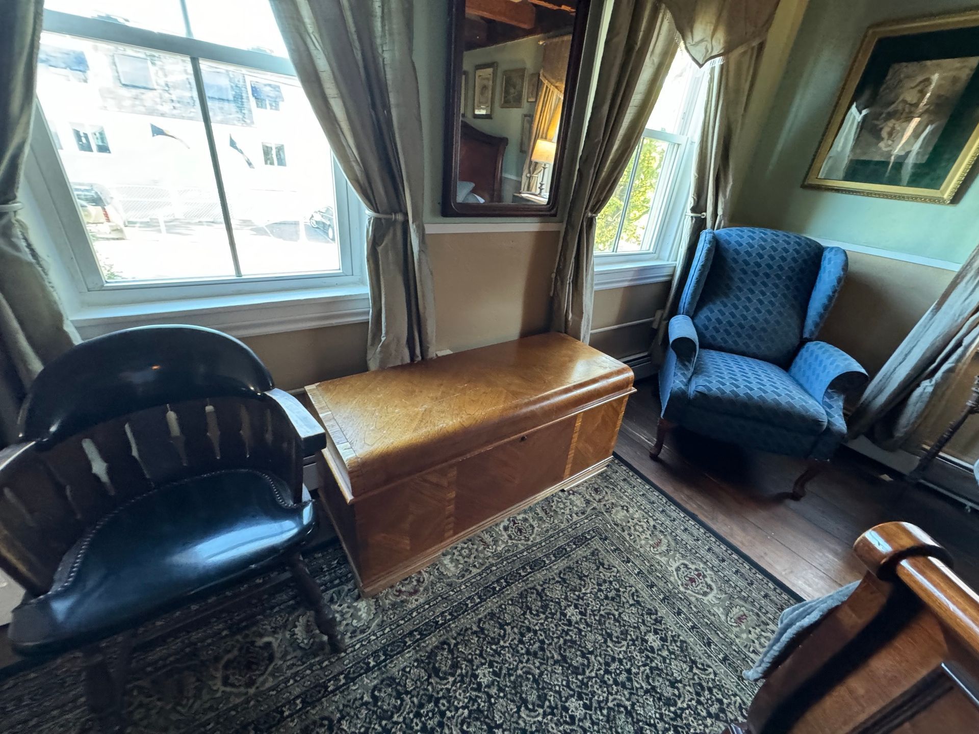 A living room with two chairs , a trunk , and a mirror.