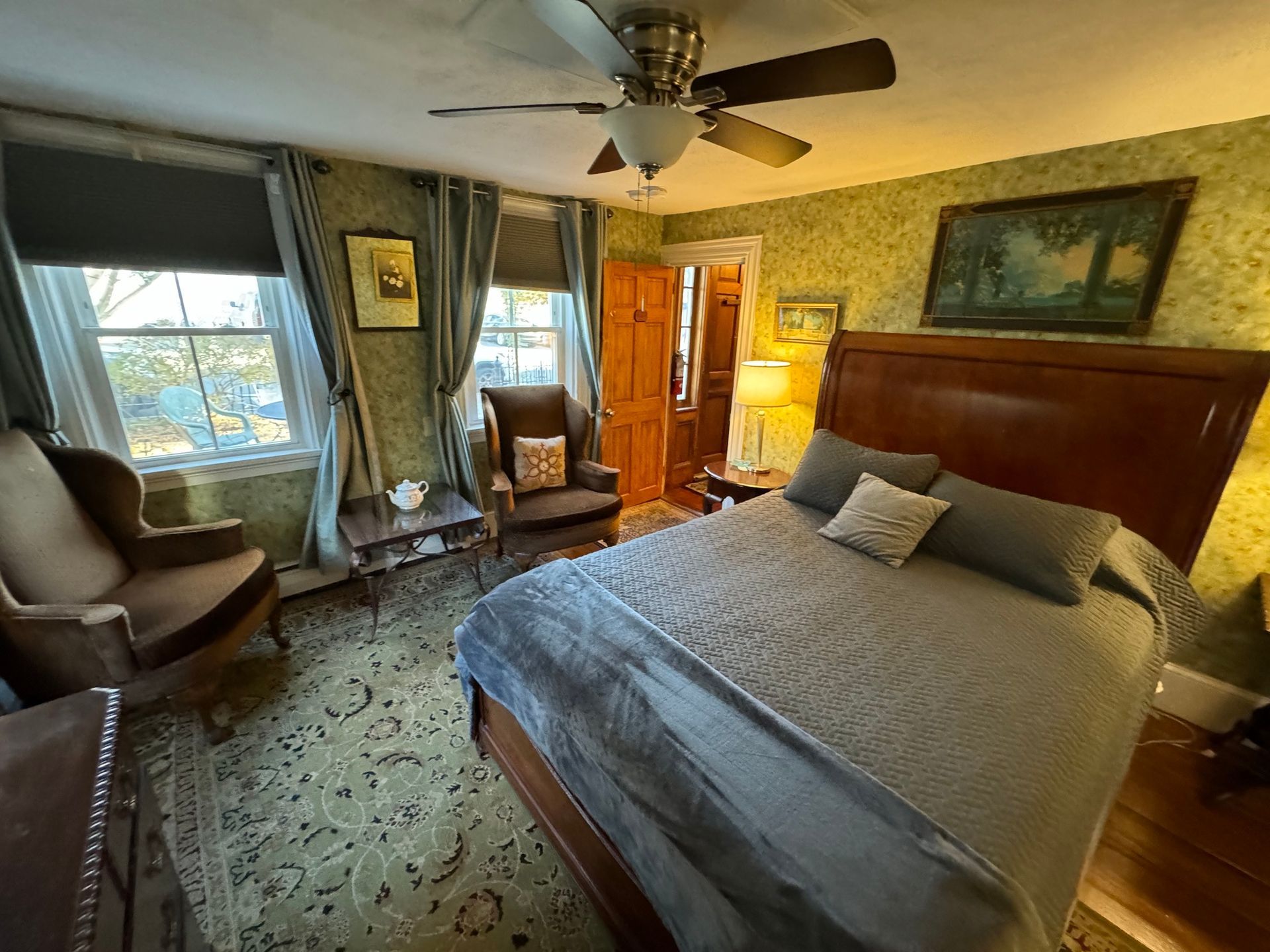 A bedroom with a bed , chair , table and ceiling fan.