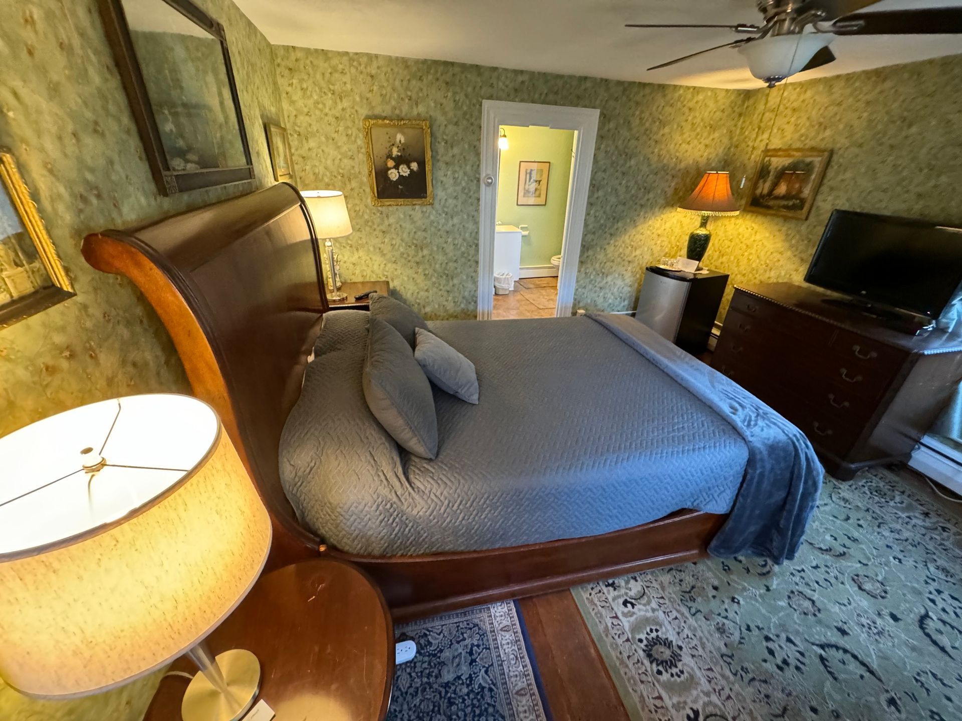 A bedroom with a king size bed , two lamps , a television and a ceiling fan.