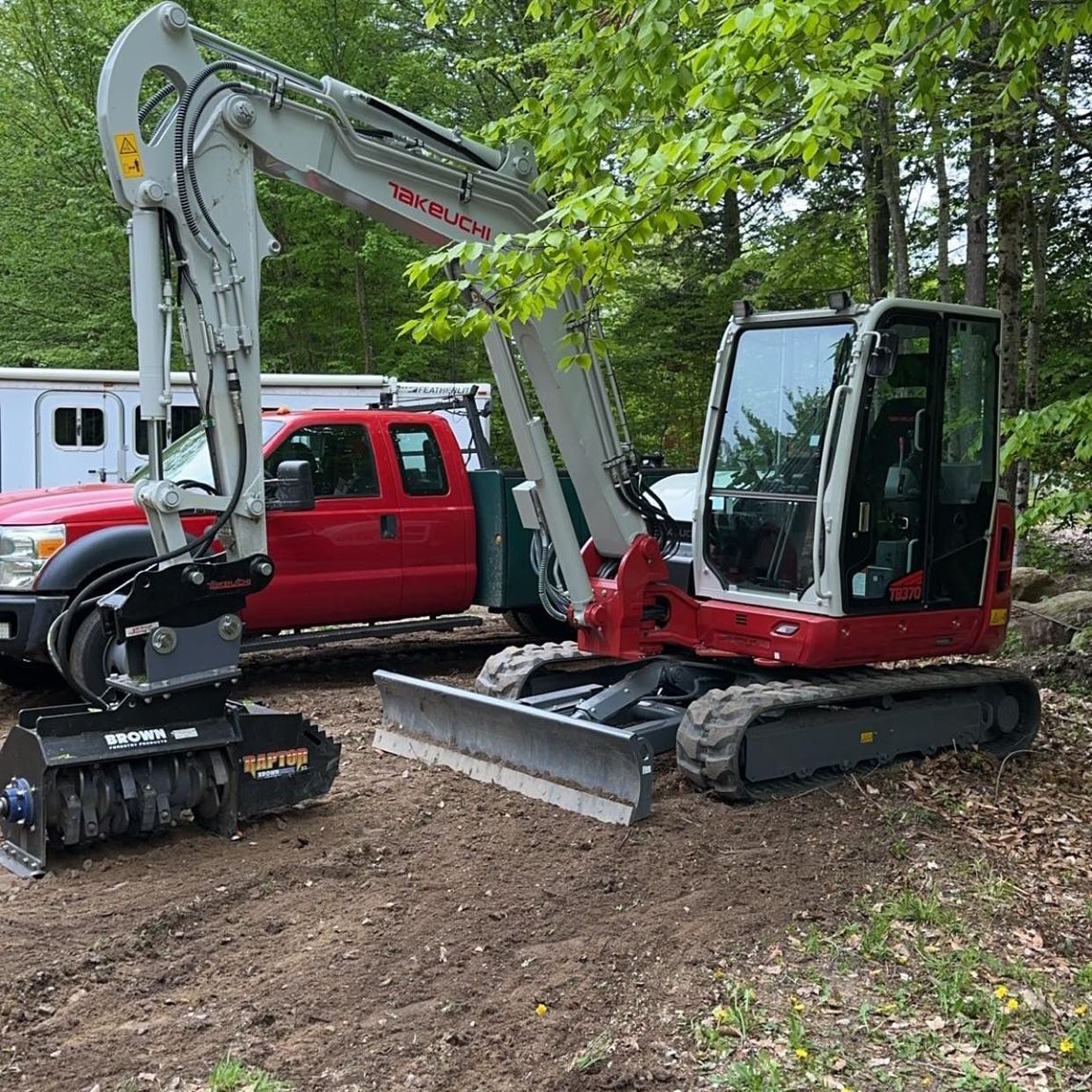 A red truck is parked next to a red excavator.