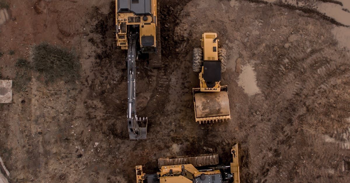 An aerial view of three construction vehicles on a dirt road.