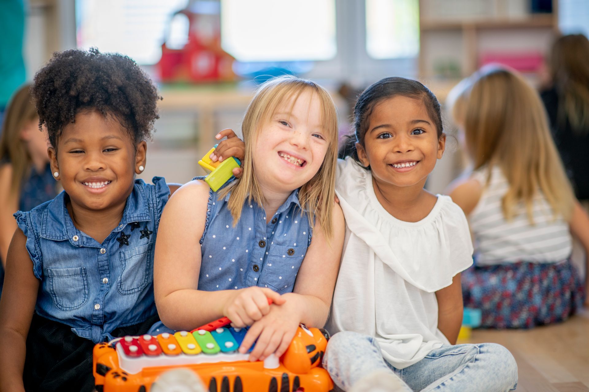 Three young girls are sitting on the floor with a toy xylophone.