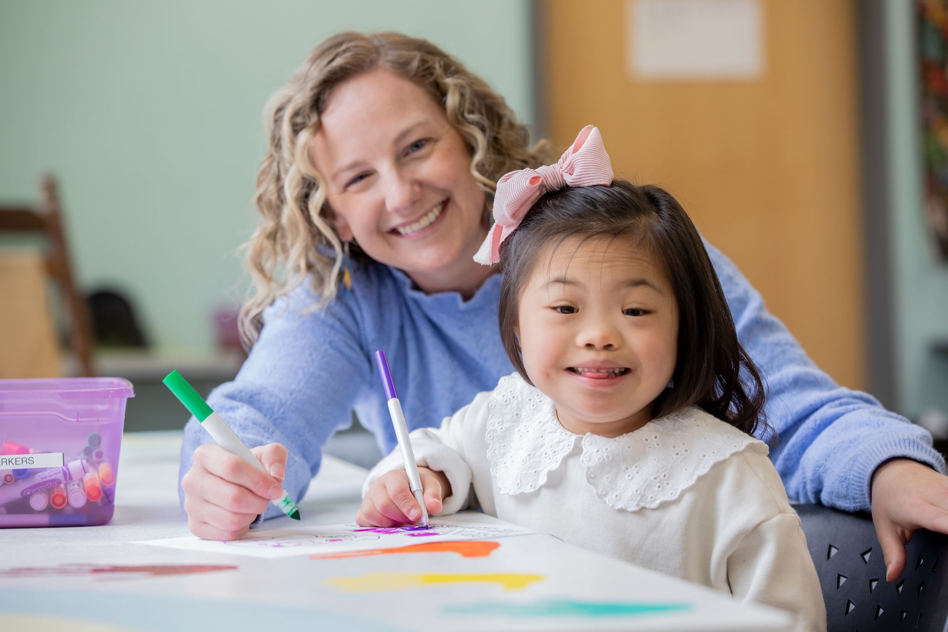 A woman and a little girl are sitting at a table drawing with markers.