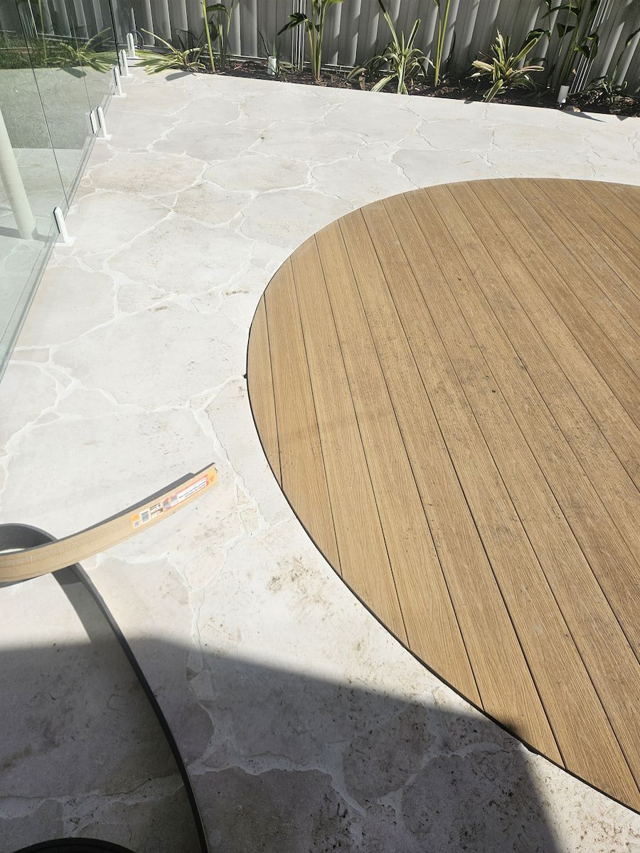 Tan, Round Outdoor Rug on Stone Patio, Chair in Foreground, Plants, Fence in Background — Kolora Projects in Robina, QLD