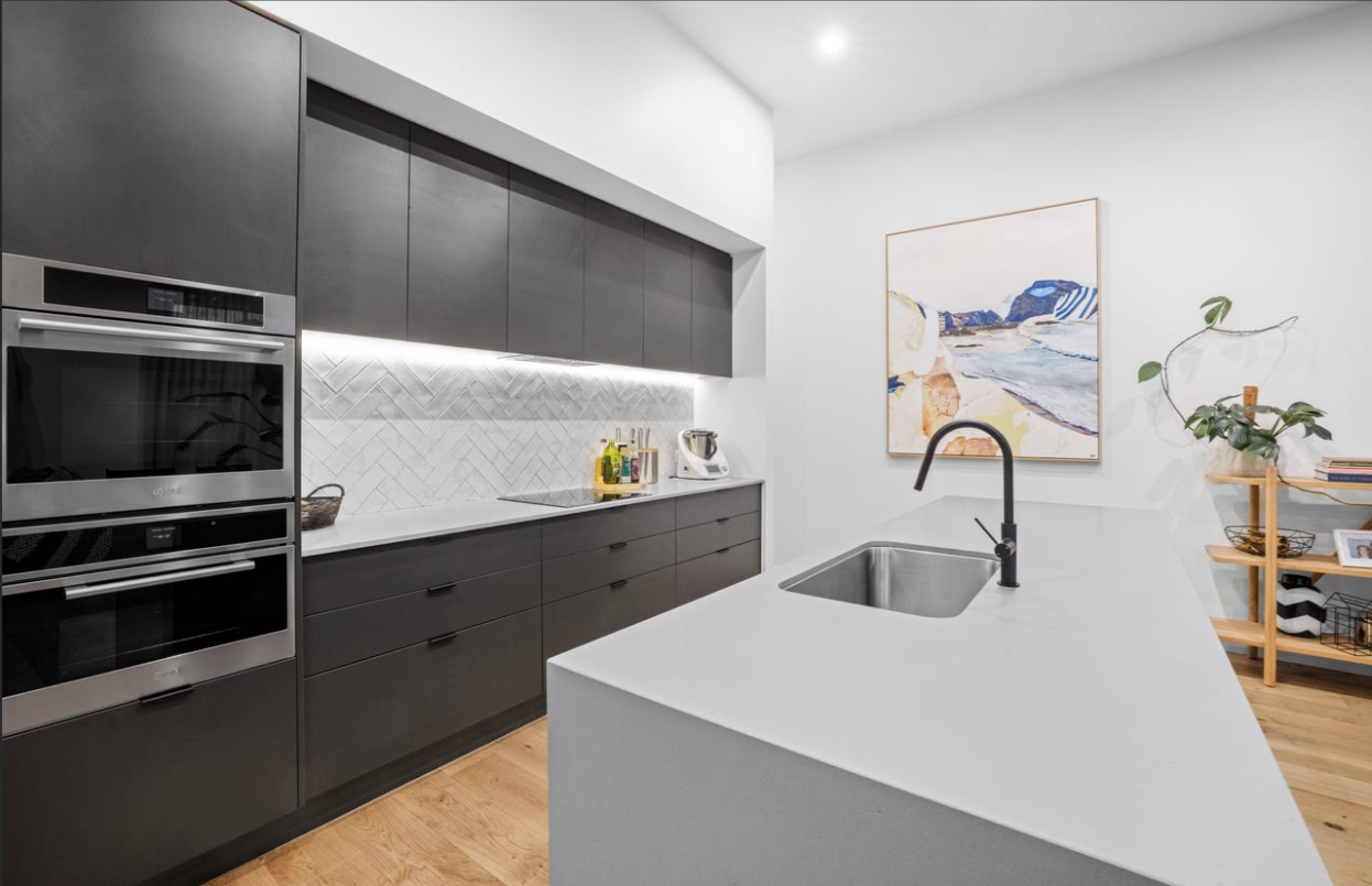 Modern kitchen with black cabinets, white countertops, and stainless steel appliances. — Kolora Projects in Robina, QLD