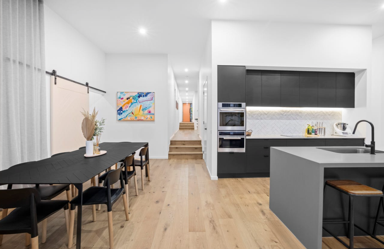 Modern Kitchen With a Black Island, Dark Cabinets, and Dining Area With a Long Black Table — Kolora Projects in Robina, QLD