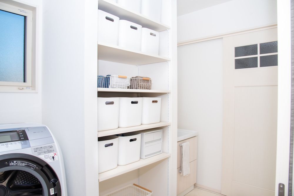 Laundry Room With Washing Machine, White Shelving With Storage Bins, and Door — Kolora Projects in Robina, QLD