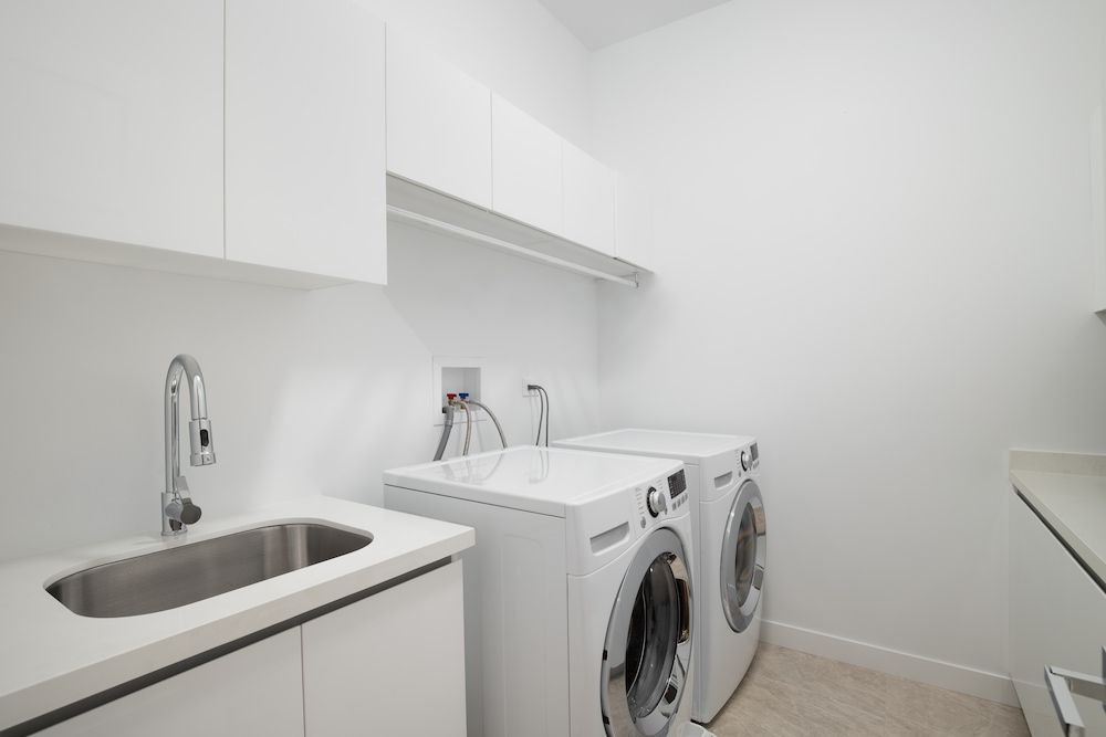 Laundry Room With White Washer and Dryer, Stainless Steel Sink, and White Cabinets — Kolora Projects in Robina, QLD