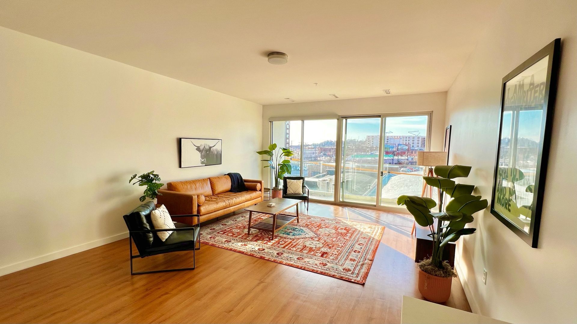 Living room with leather sofa, rug, and large windows overlooking city view.