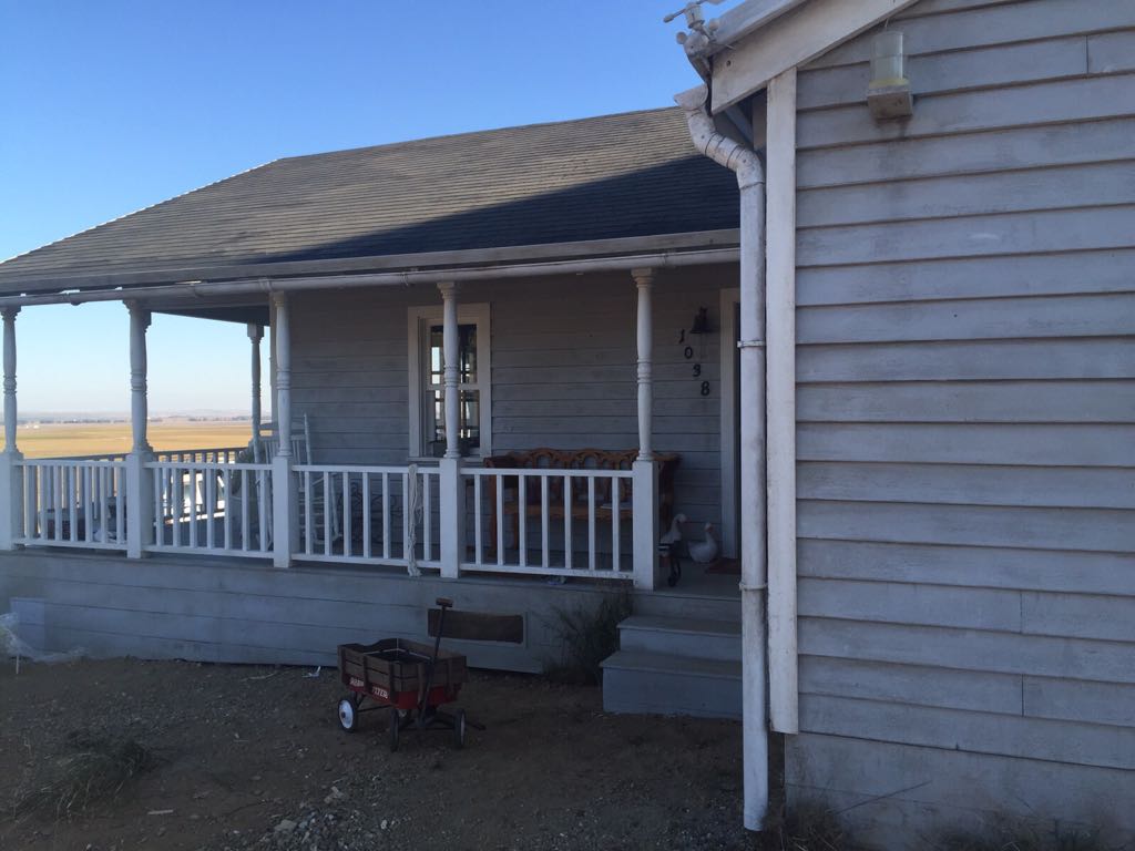 Una casa blanca con un porche y un carro rojo delante de ella.