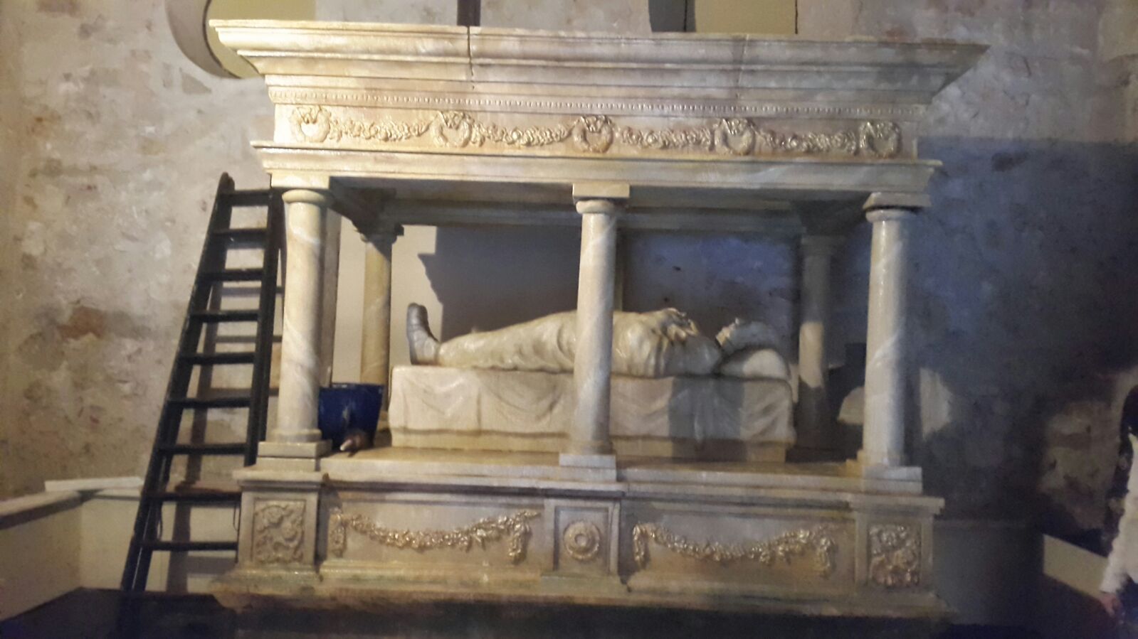 Una estatua de un hombre acostado en una cama con una escalera al lado.