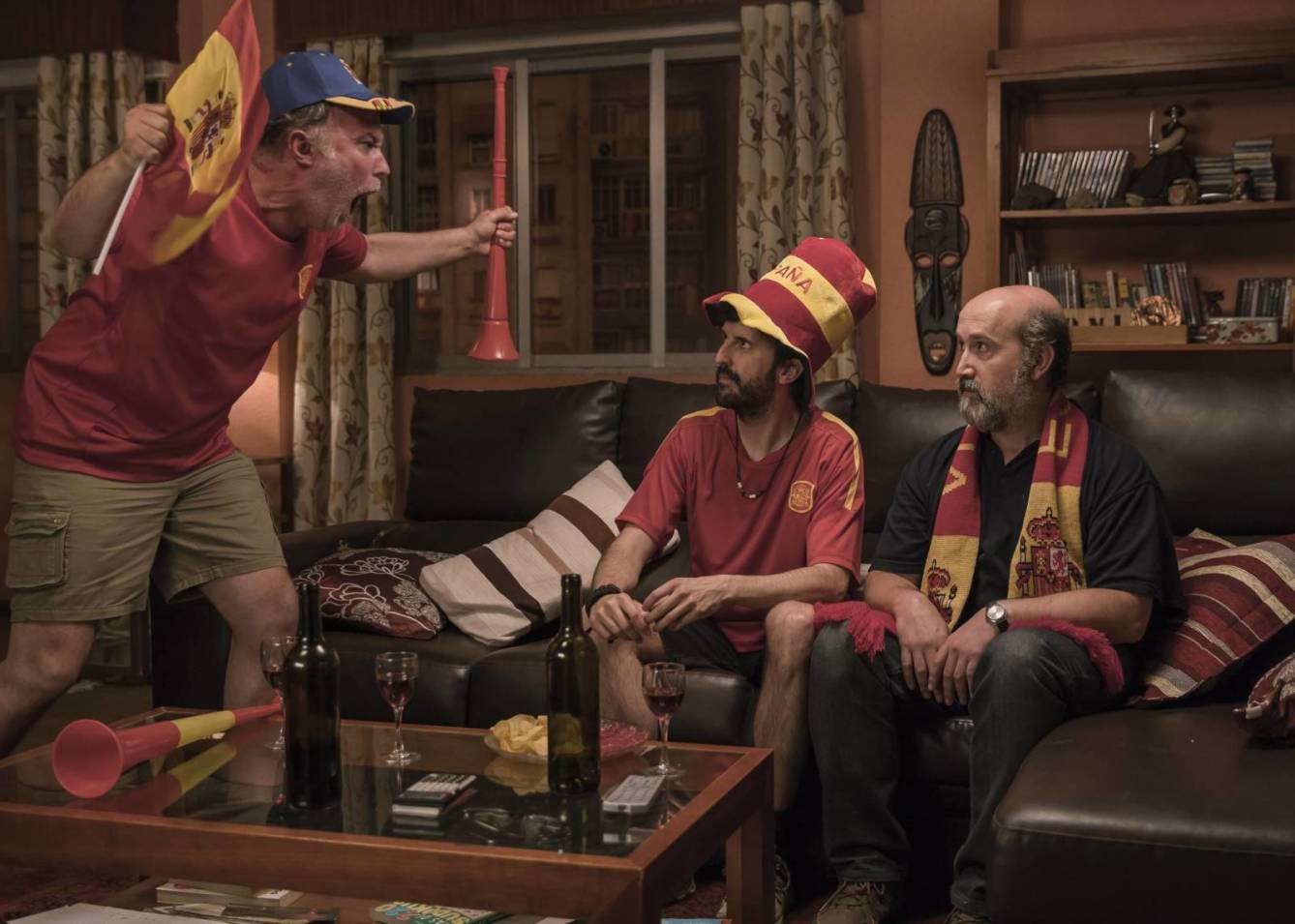 Un grupo de hombres está sentado en un sofá viendo un partido de fútbol.