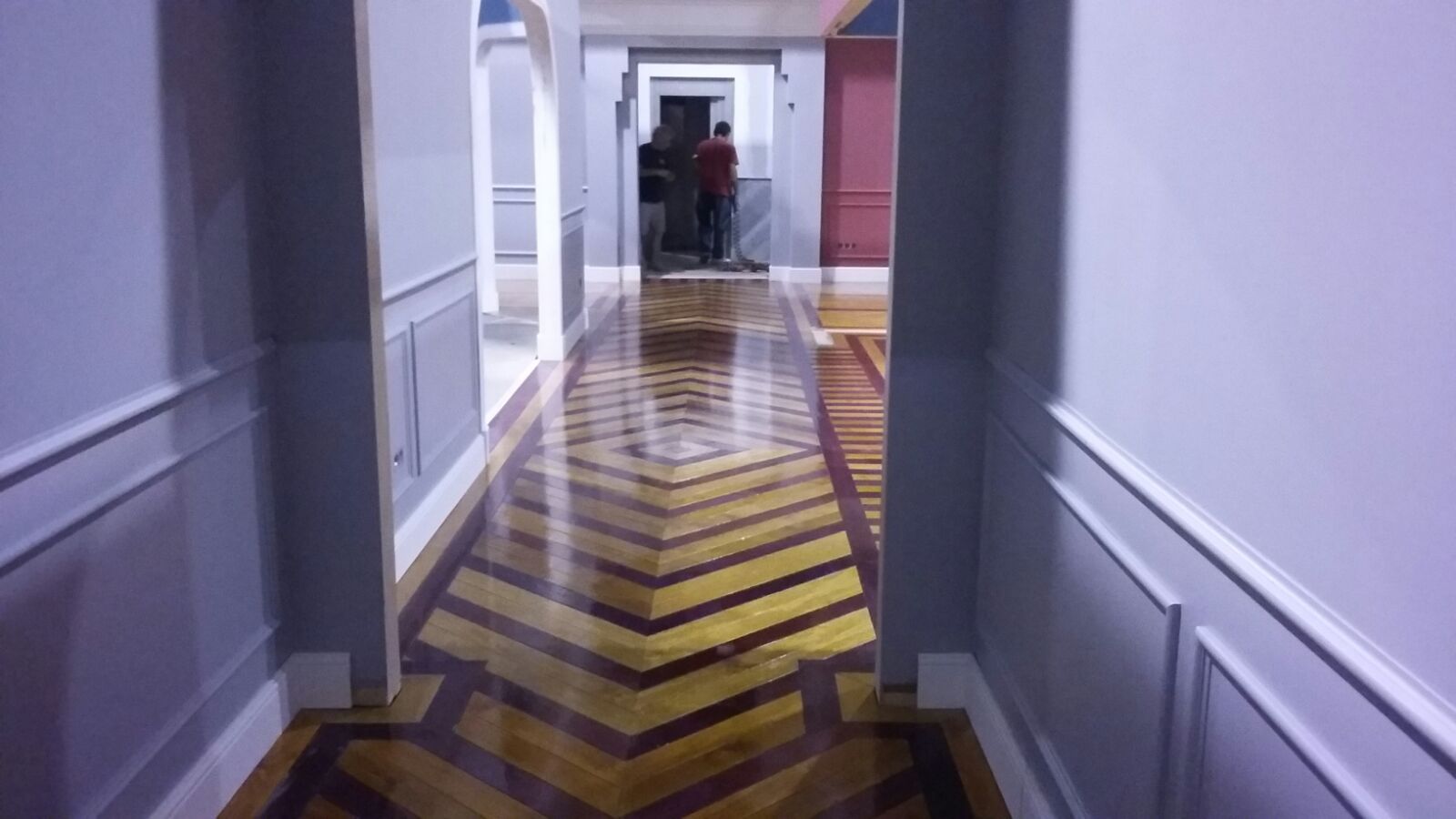 Un largo pasillo con suelo de madera y una pared morada.