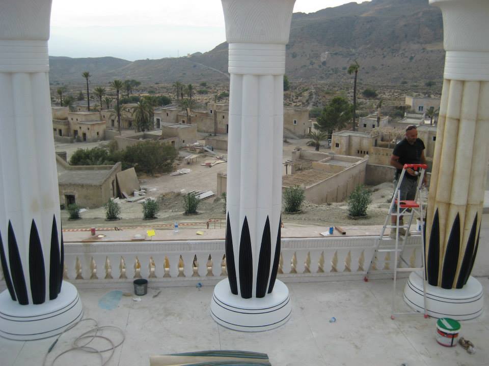 Un hombre en una escalera pinta un pilar en un balcón.