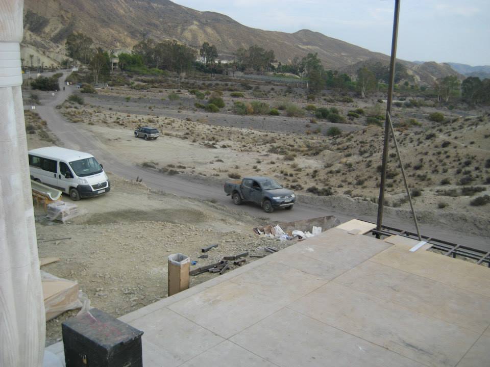 Un coche circula por un camino de tierra con montañas al fondo.