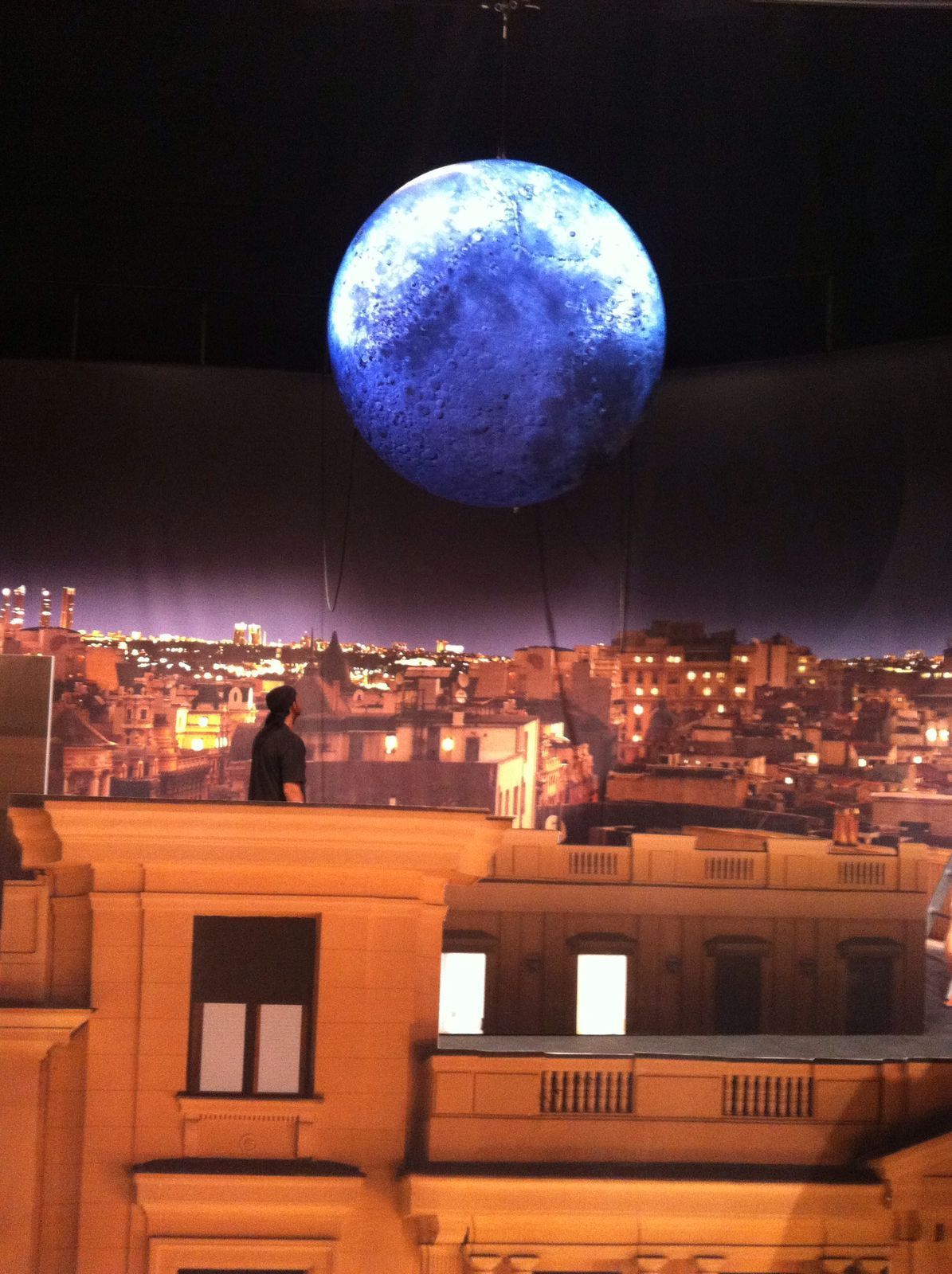 Un hombre está parado en el techo de un edificio mirando una luna azul.