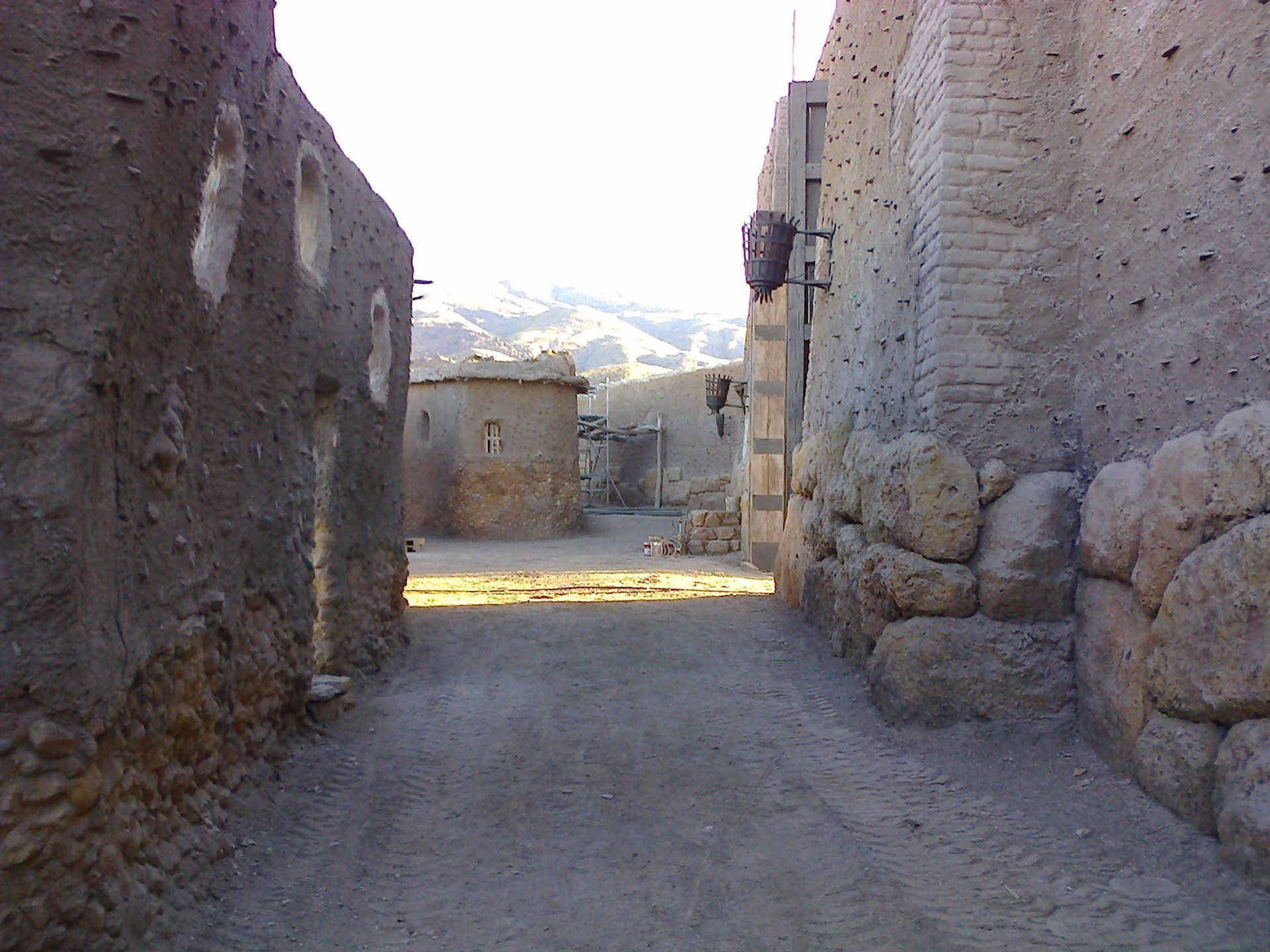Un callejón estrecho entre dos edificios de piedra con montañas al fondo.